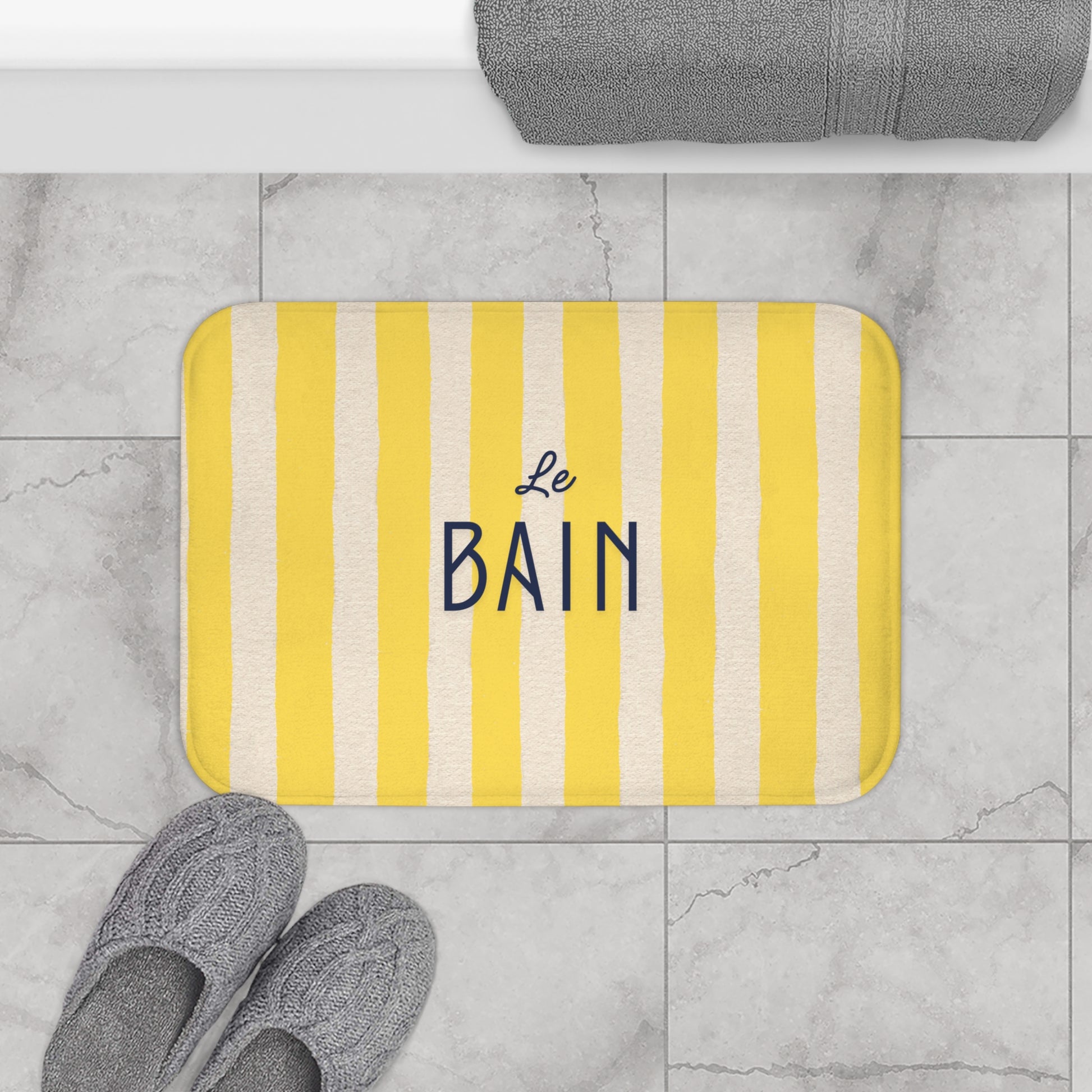 Yellow and white striped bath mat with 'Le Bain' text on a tiled bathroom floor.