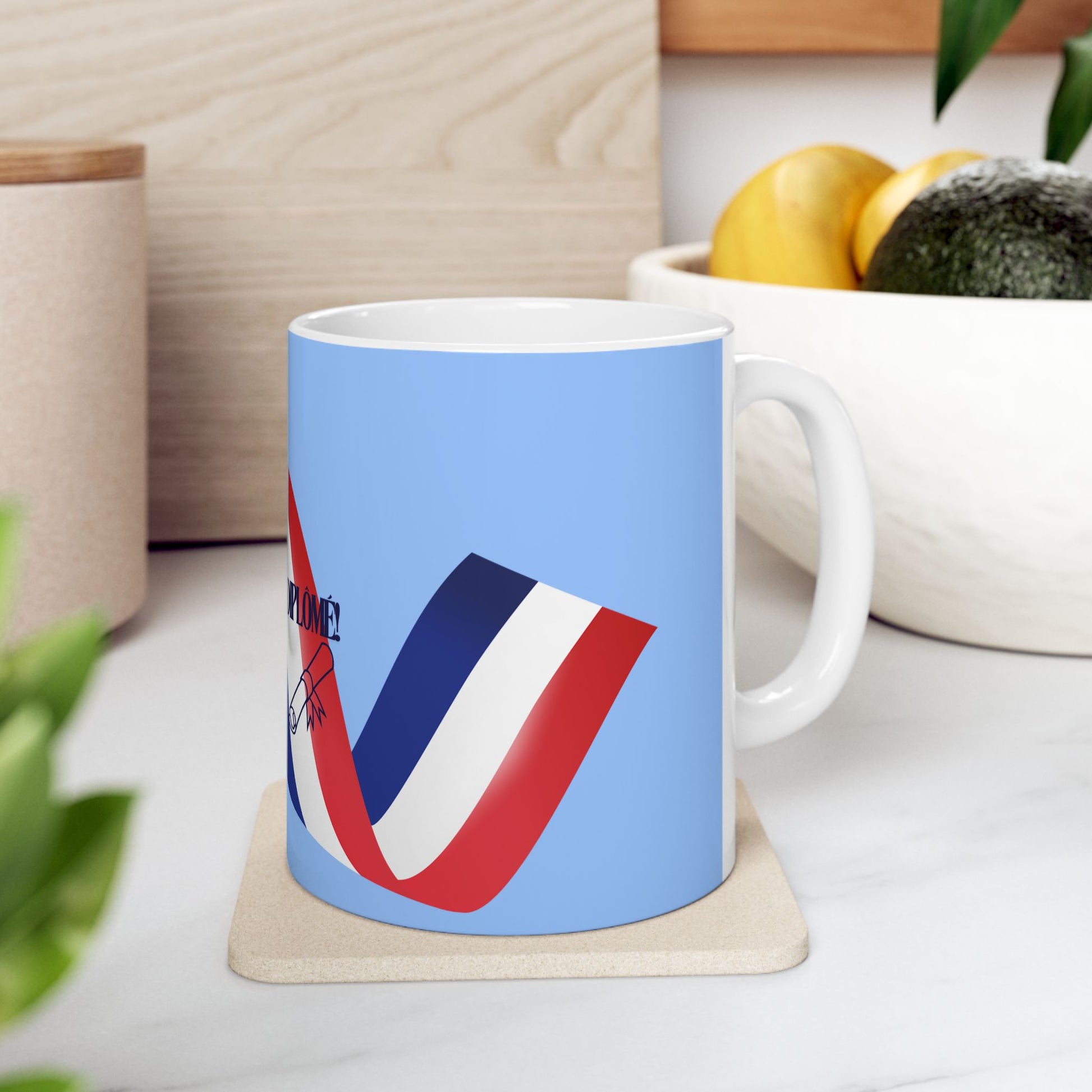 Mug with a colorful design on a coaster, placed on a surface with a plant and container in the background.
