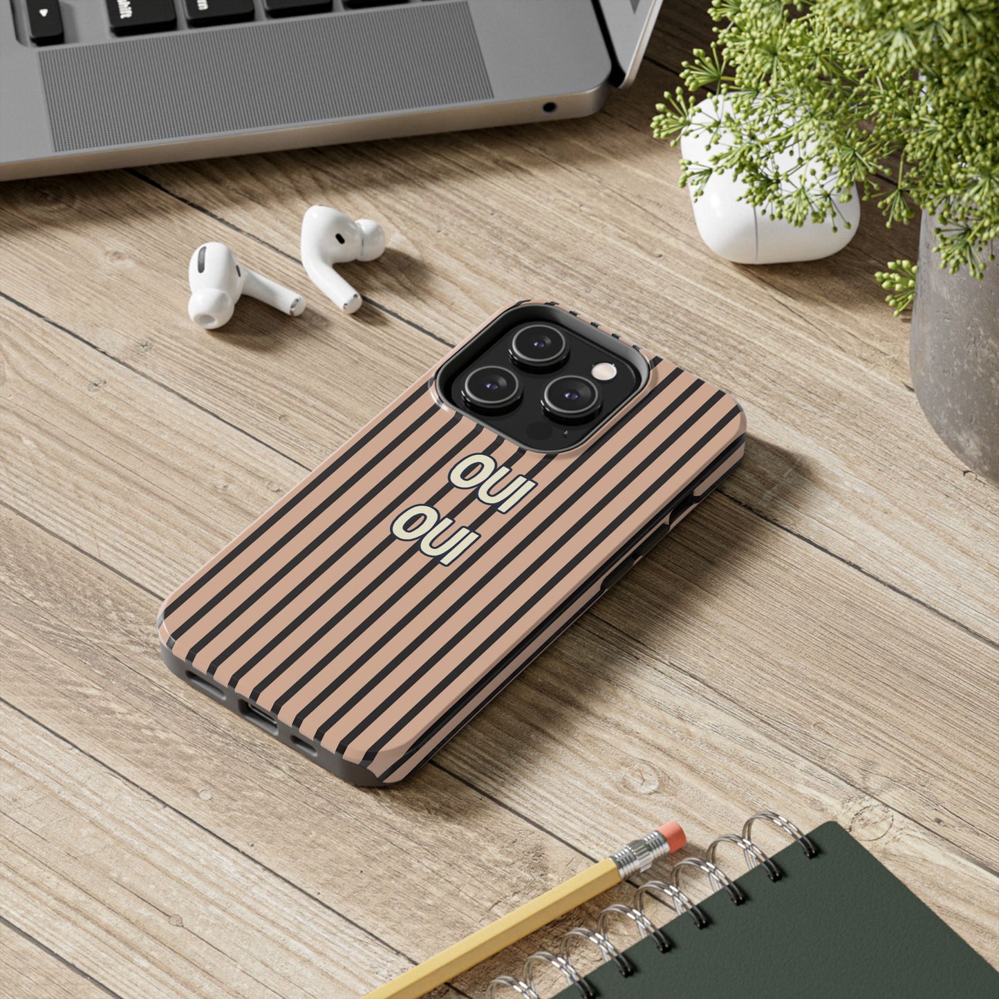 Phone case with 'OU' text on a wooden surface with laptop, earbuds, and notebook.