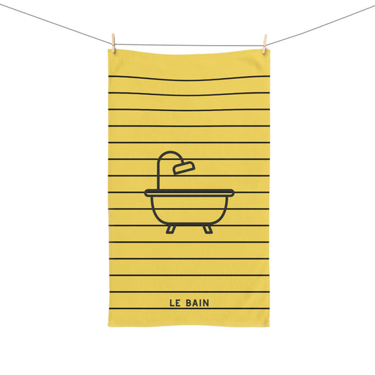 A yellow kitchen towel with black horizontal stripes and a black line-art illustration of a bathtub with a faucet. The words 'LE BAIN' are printed at the bottom.
