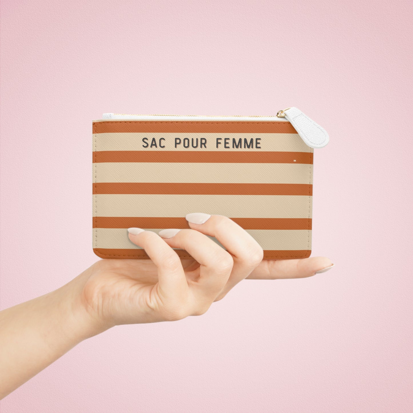 Hand holding a striped pouch labeled 'SAC POUR FEMME' against a pink background