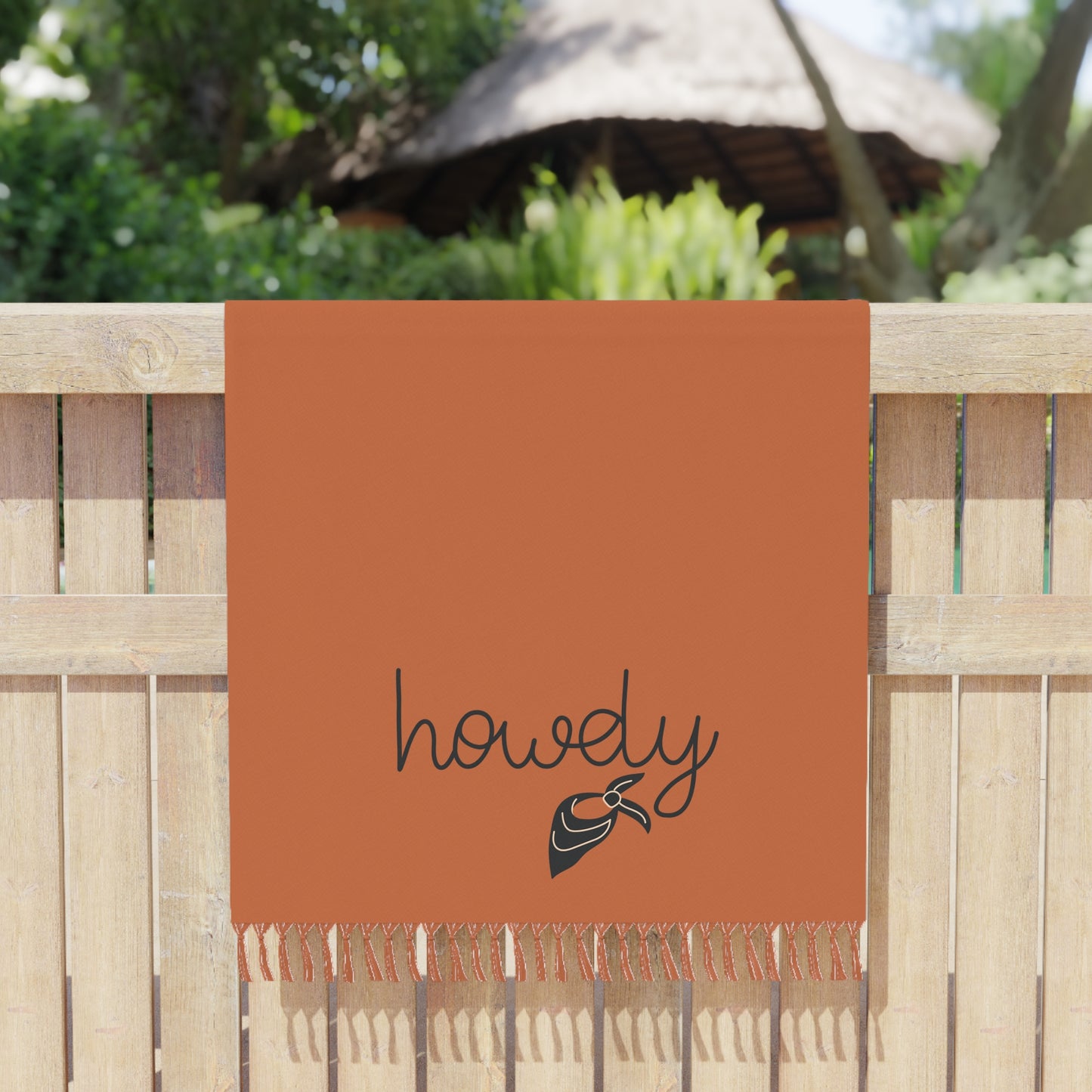 Orange towel with 'howdy' and a bow design hanging on a wooden fence.