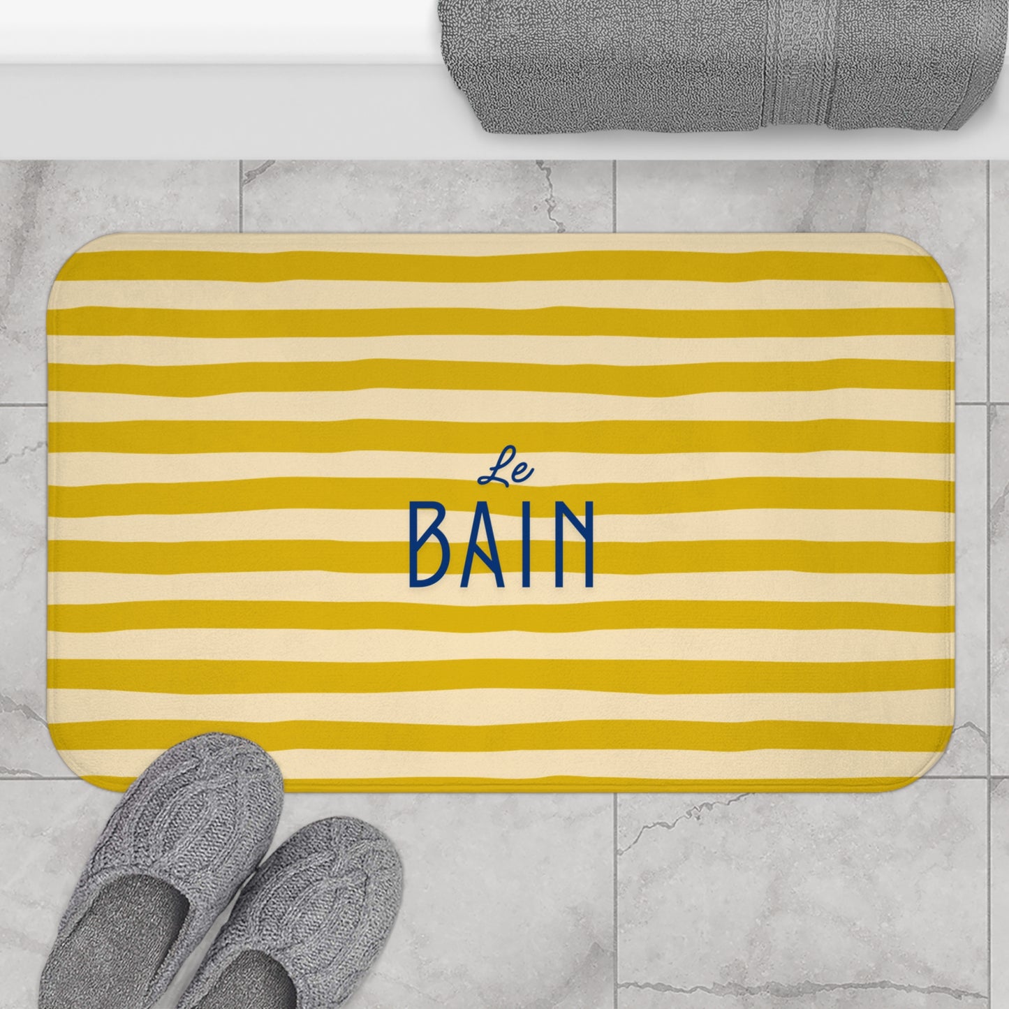 Yellow striped bath mat with 'Le Bain' text on a marble floor.