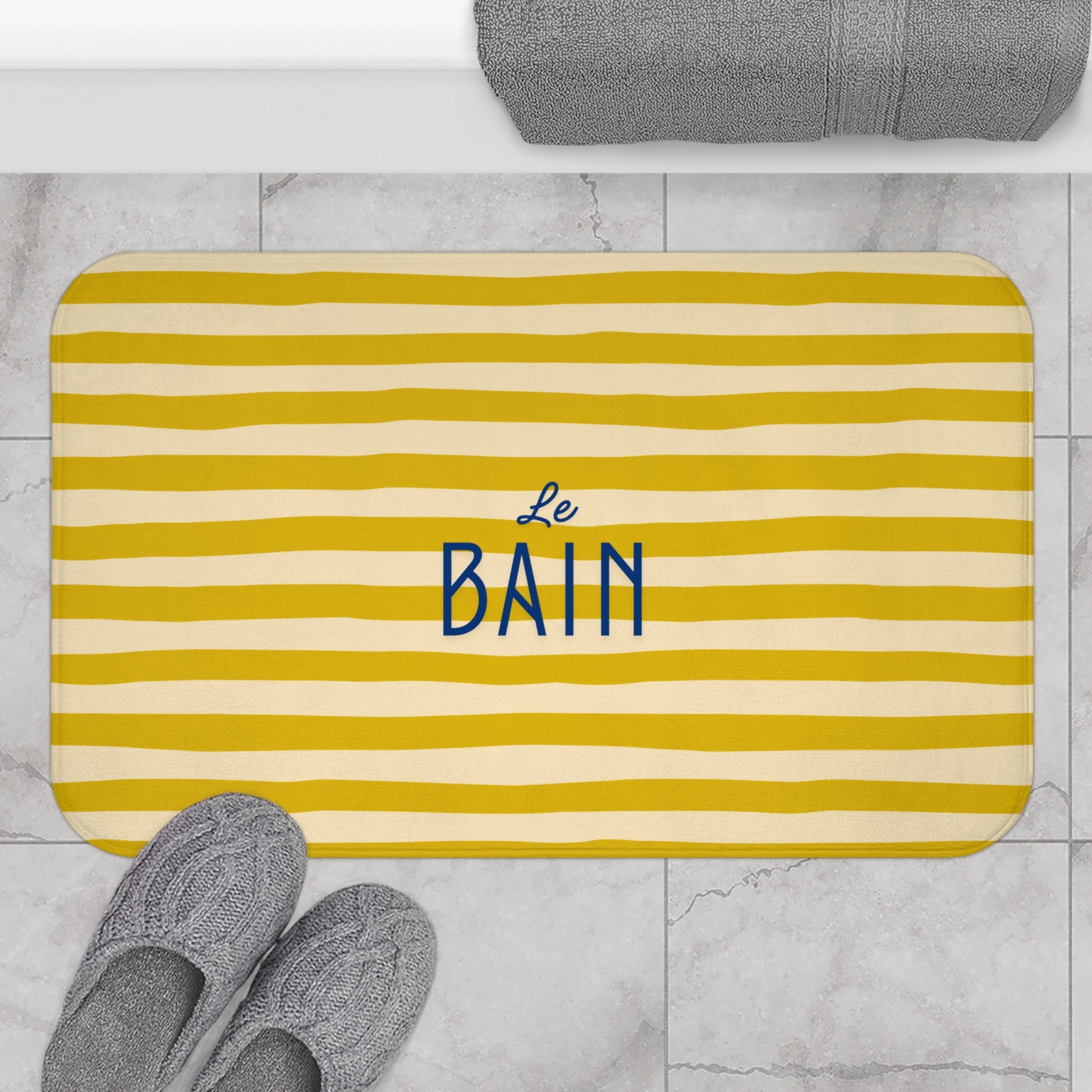 Yellow striped bath mat with 'Le Bain' text on a marble floor.