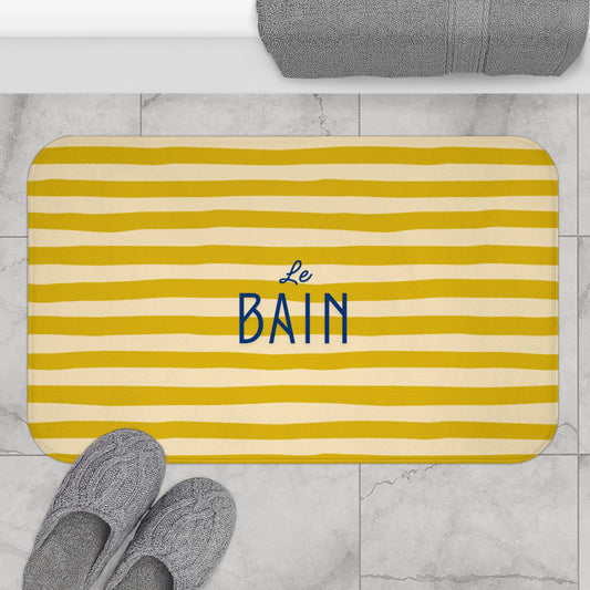 Yellow striped bath mat with 'Le Bain' text on a marble floor.