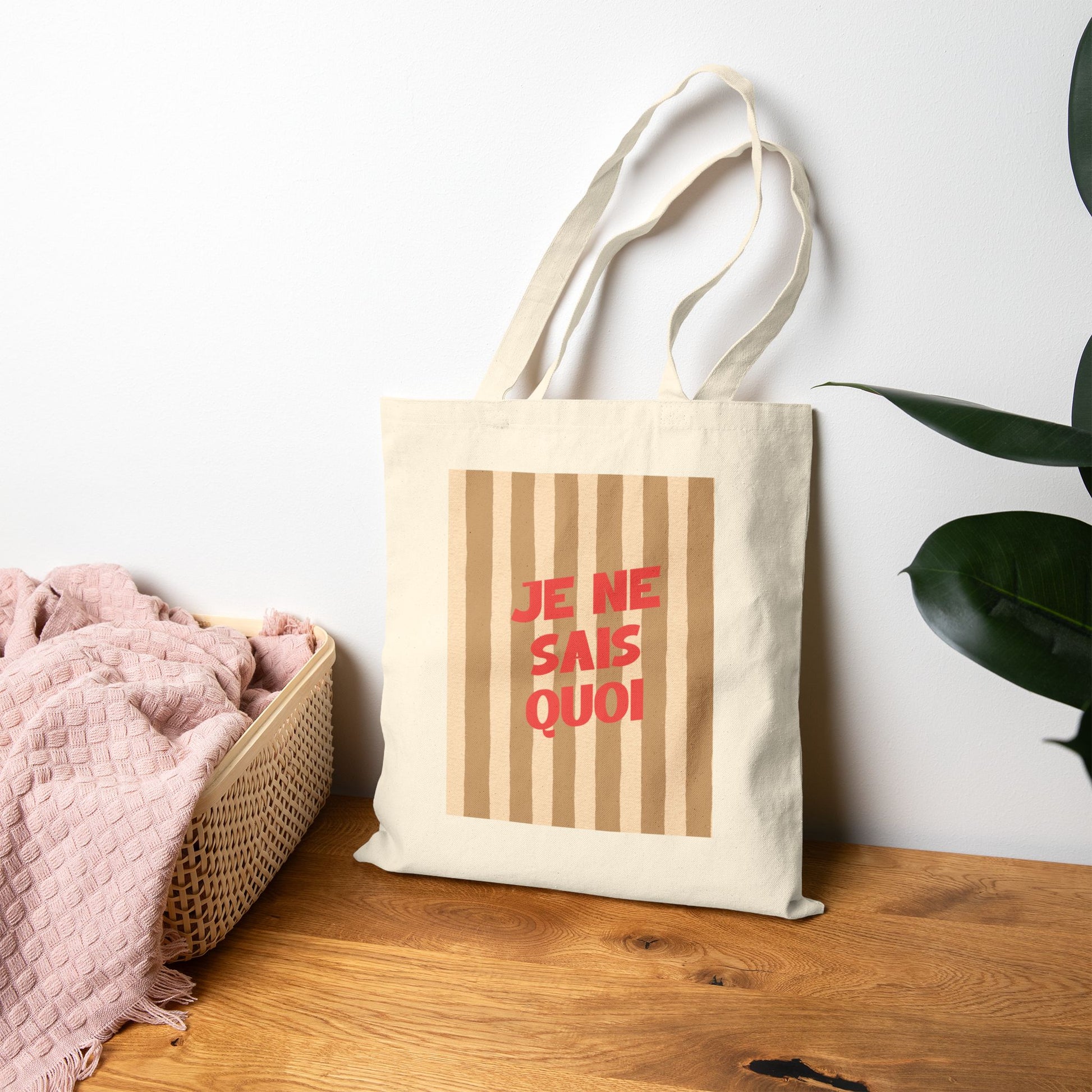 Tote bag with 'JE NE SAIS QUOI' text on a wooden surface with a plant in the background