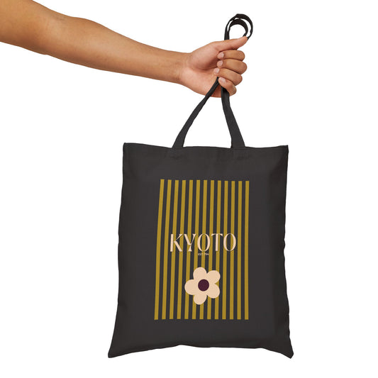 Black tote bag with 'KYOTO' and a flower design held by a hand on a white background