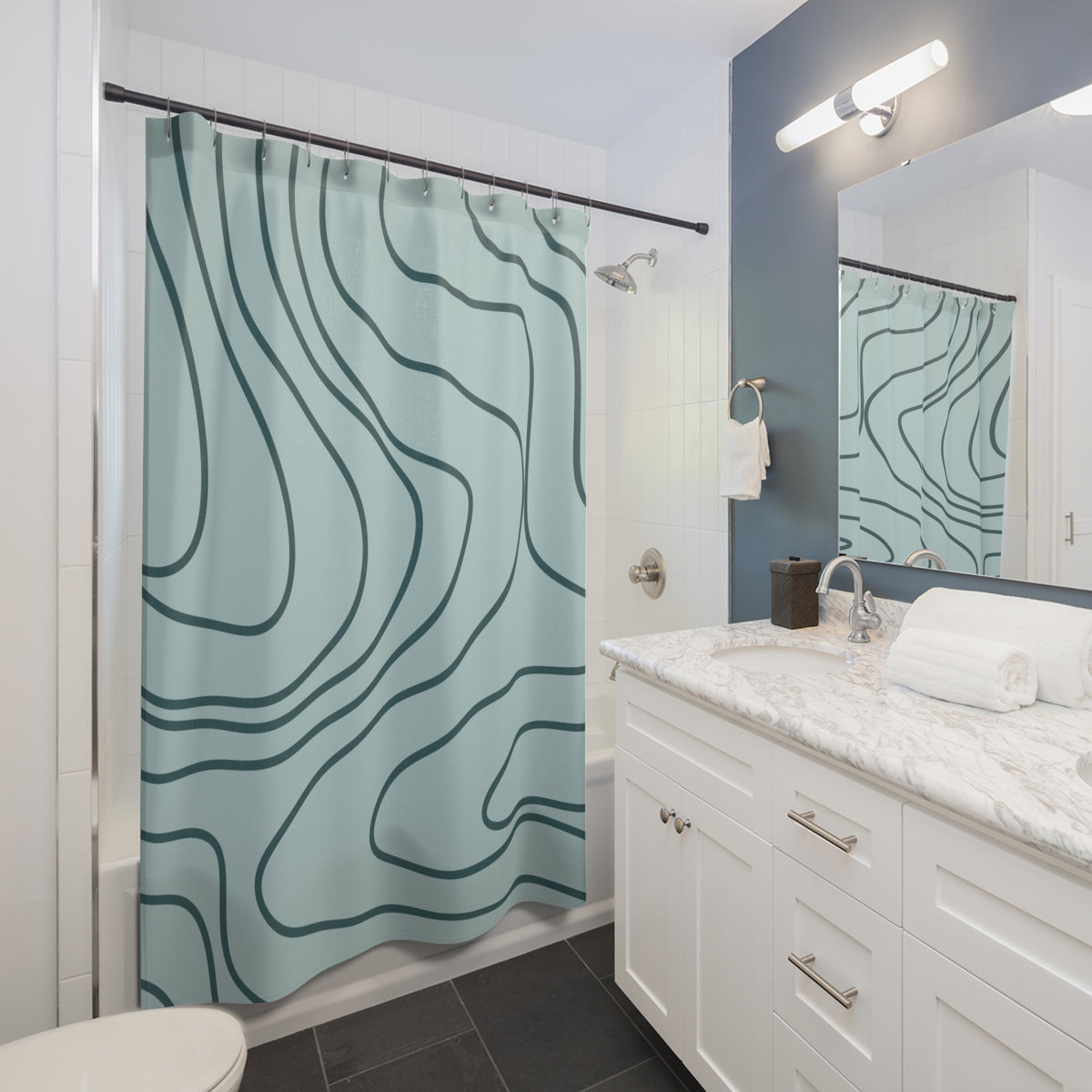 A modern bathroom featuring a light blue shower curtain with a dark teal topographic line pattern. The bathroom includes a white vanity with a marble countertop, a large mirror, and a blue accent wall.