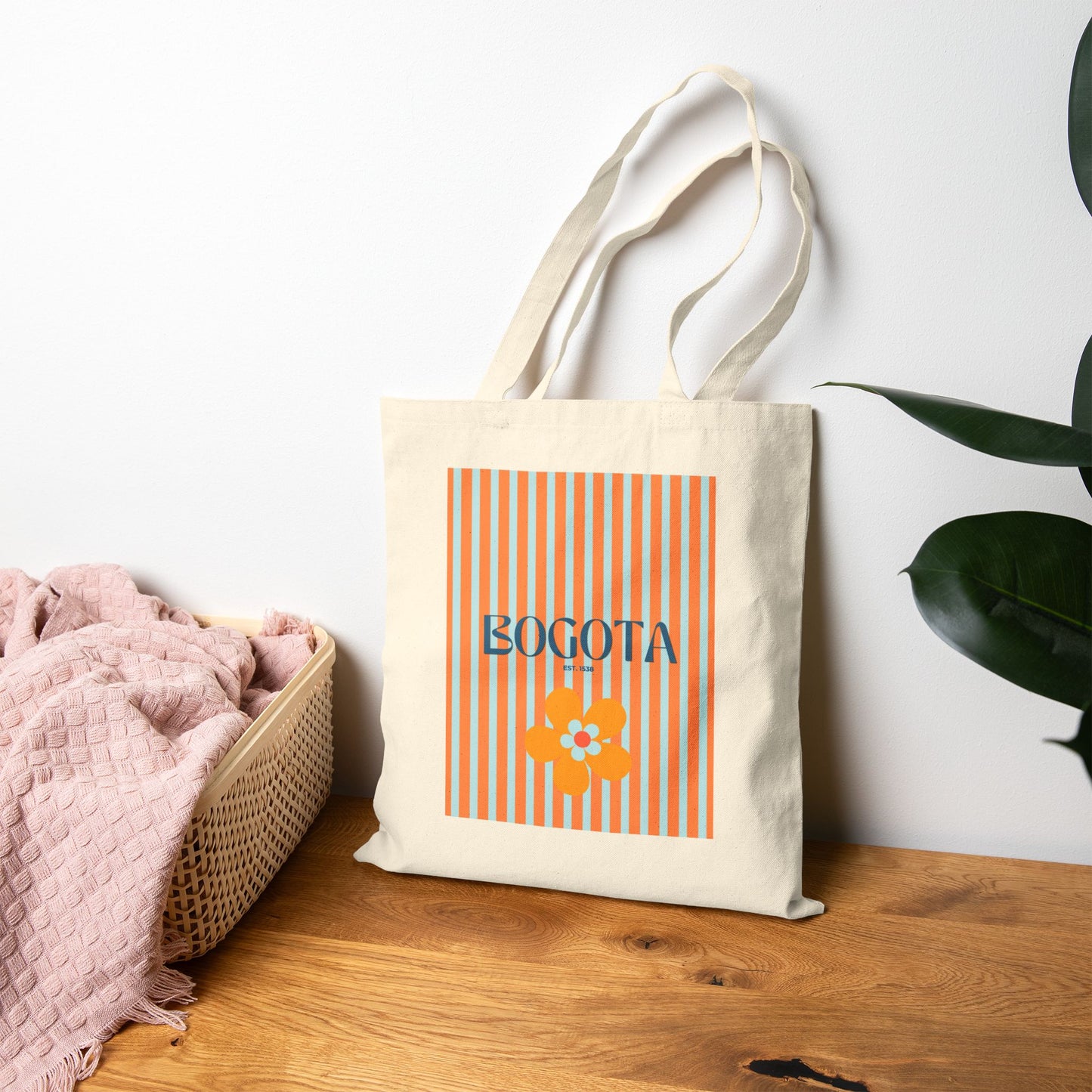 Tote bag with 'Bogota' design on a wooden surface with a white wall and plant in the background