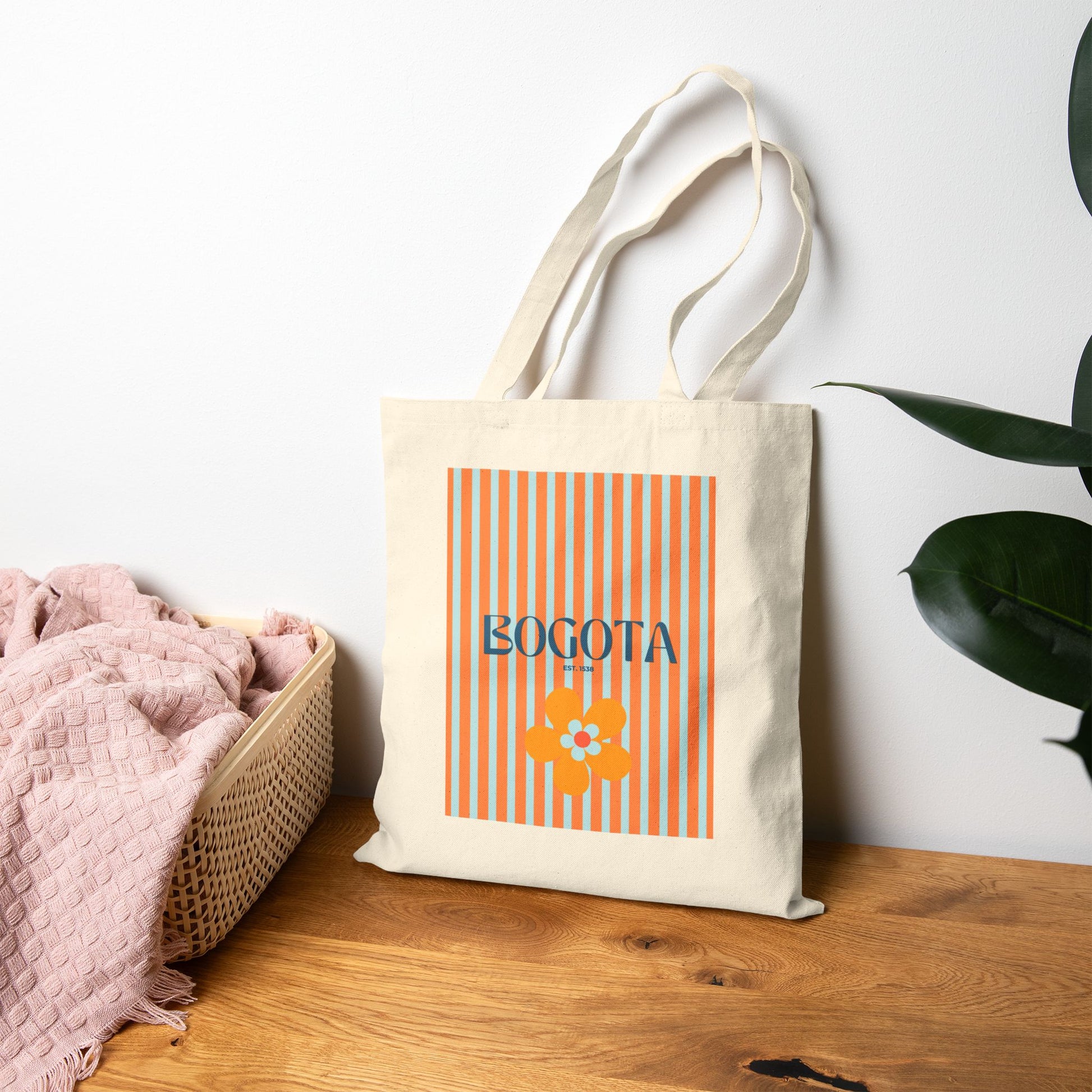 Tote bag with 'Bogota' design on a wooden surface with a white wall and plant in the background