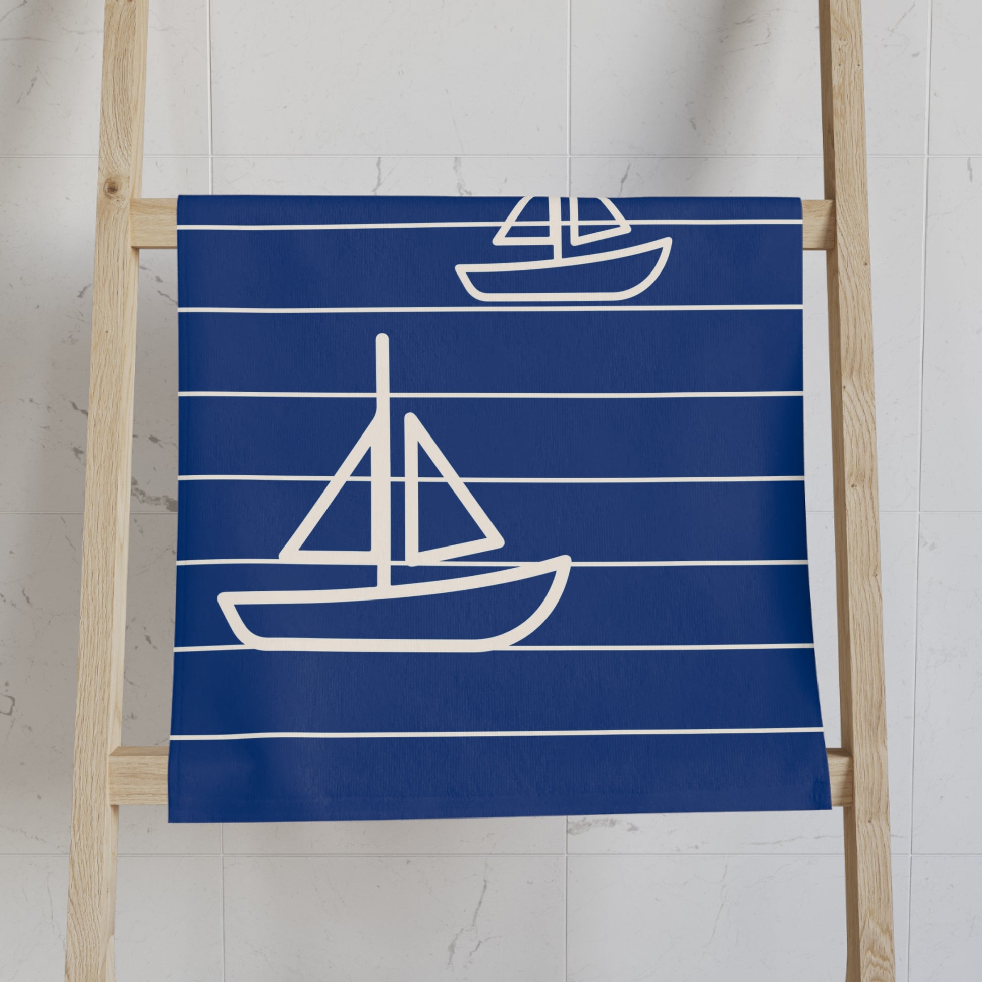 Navy blue towel with white sailboat designs on a wooden ladder against a white wall.