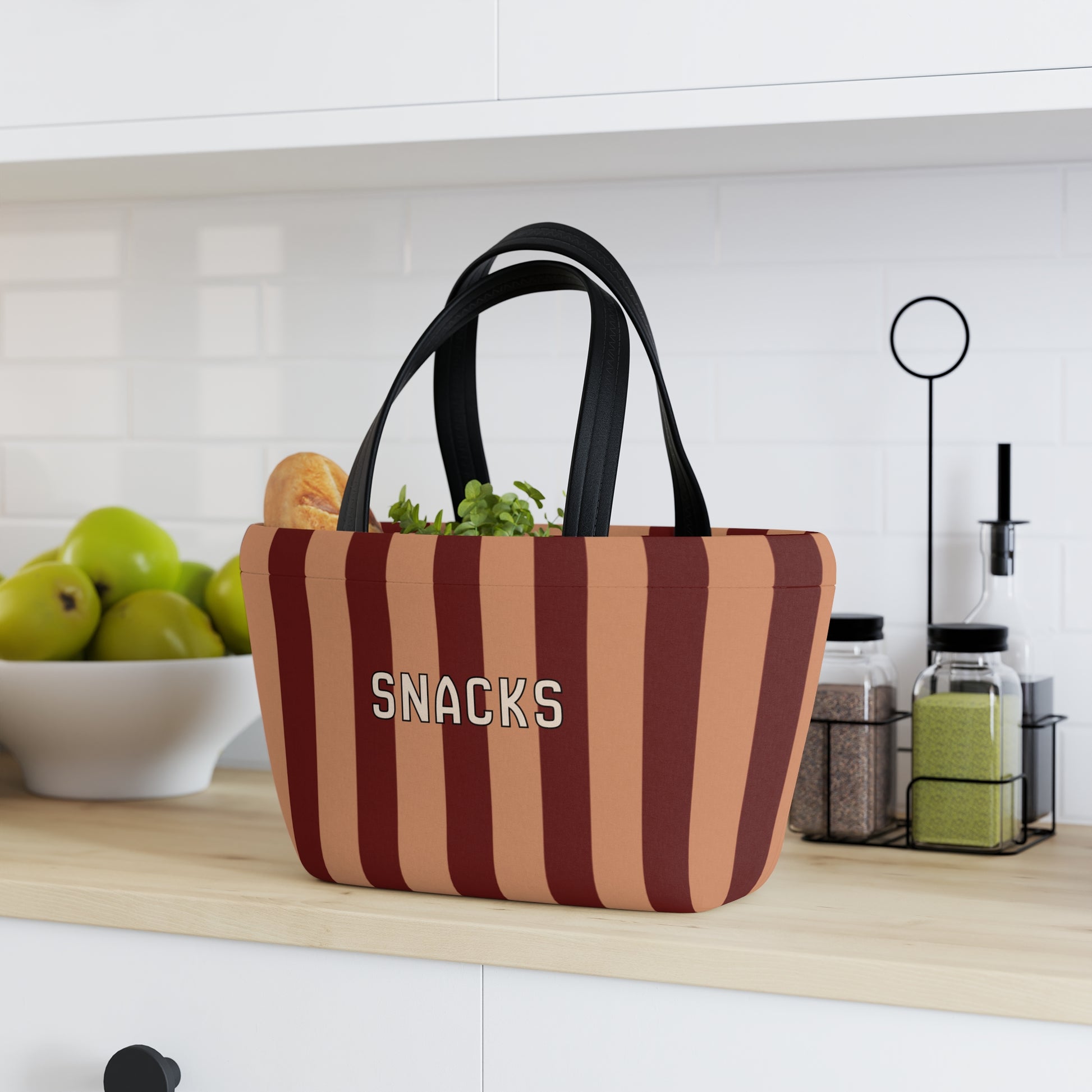 Striped snack bag labeled 'SNACKS' on a kitchen counter with fruits and kitchen items in the background.