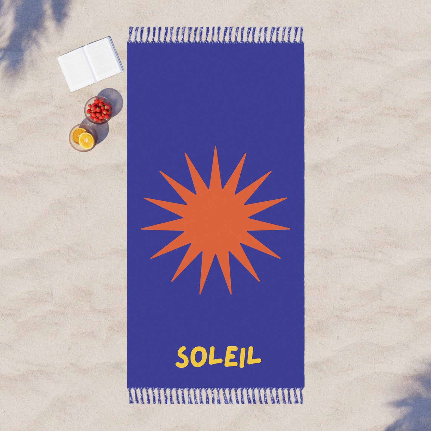 Blue beach towel with orange sun design and 'Soleil' text on a sandy background