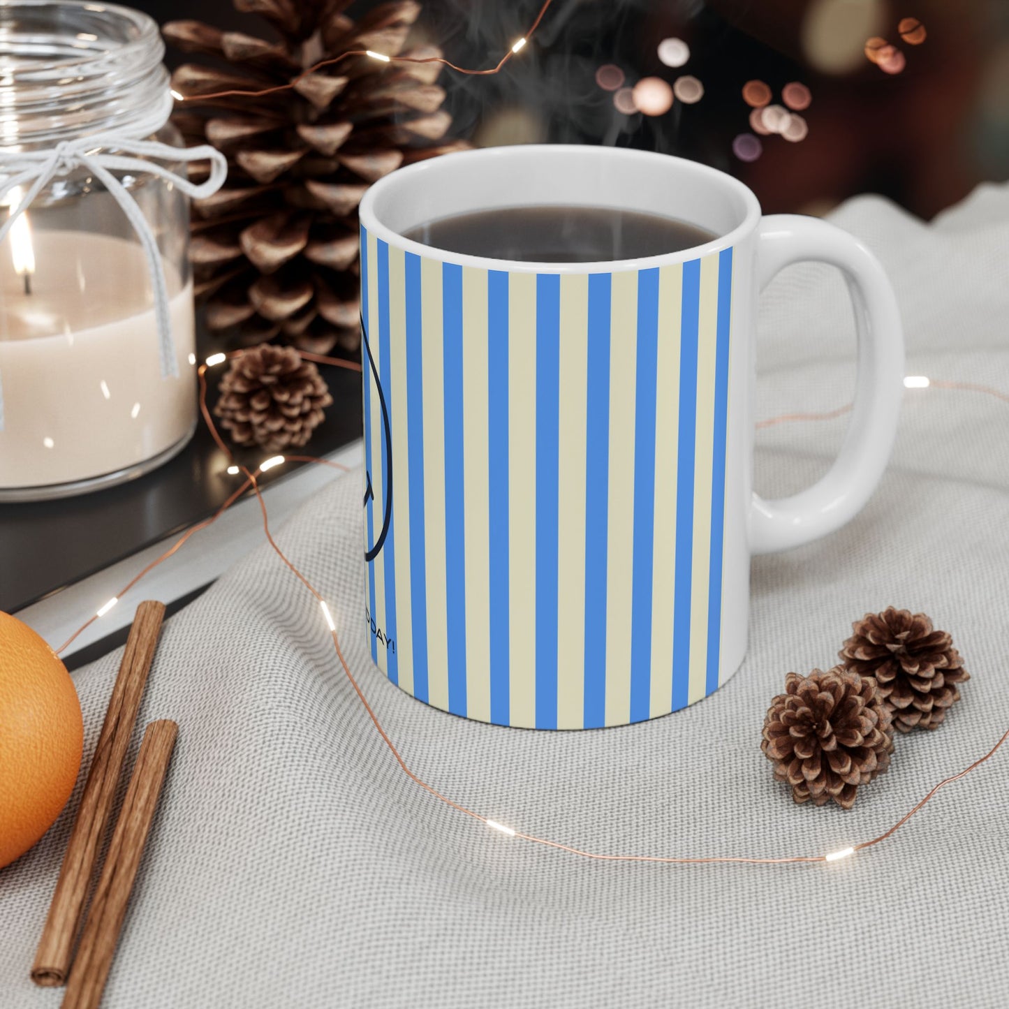 Striped mug with a candle, cinnamon sticks, and pine cones on a table.