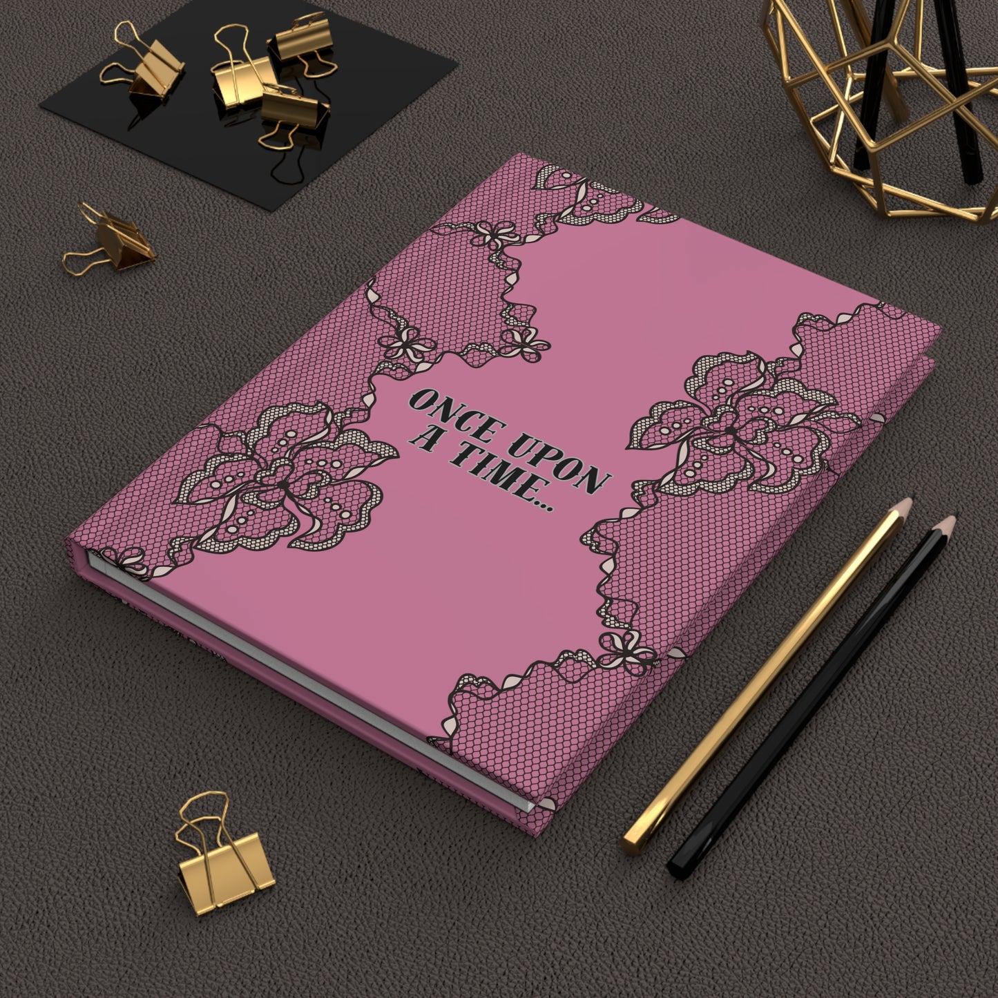 Pink notebook with lace design and 'Once Upon a Time' text on a dark surface with stationery items.