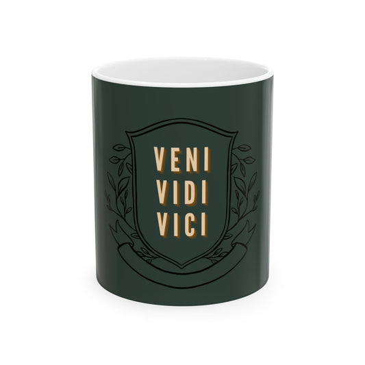 A dark green ceramic mug with a white interior, featuring a black shield emblem with the words 'VENI VIDI VICI' in gold lettering and decorative leaf motifs.
