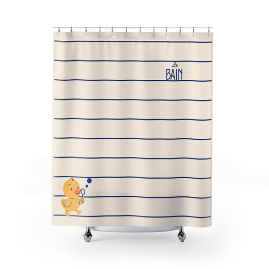A cream-colored shower curtain with horizontal navy blue stripes, featuring a small yellow duck blowing bubbles in the lower left and the word 'BAIN' in navy blue in the upper right.