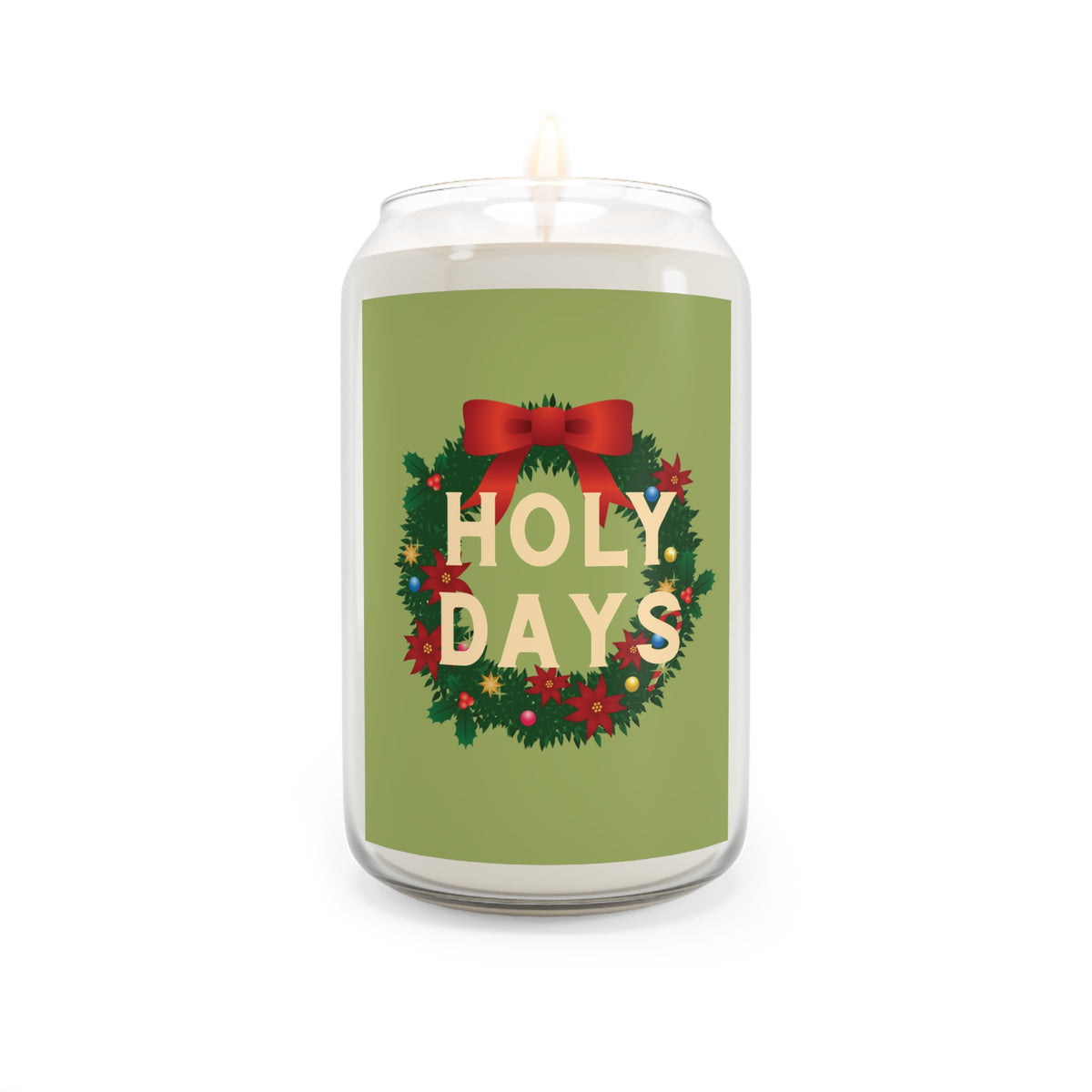 A white wax candle in a clear glass jar with a green holiday wreath label that reads 'HOLY DAYS' in cream letters, accented with a red bow and small colorful ornaments. The candle is lit with a small flame against a plain white background.