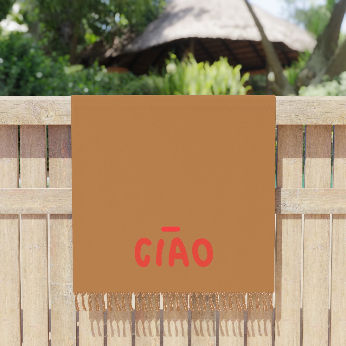 Brown towel with red text 'GIÓO' hanging on a wooden fence outdoors.