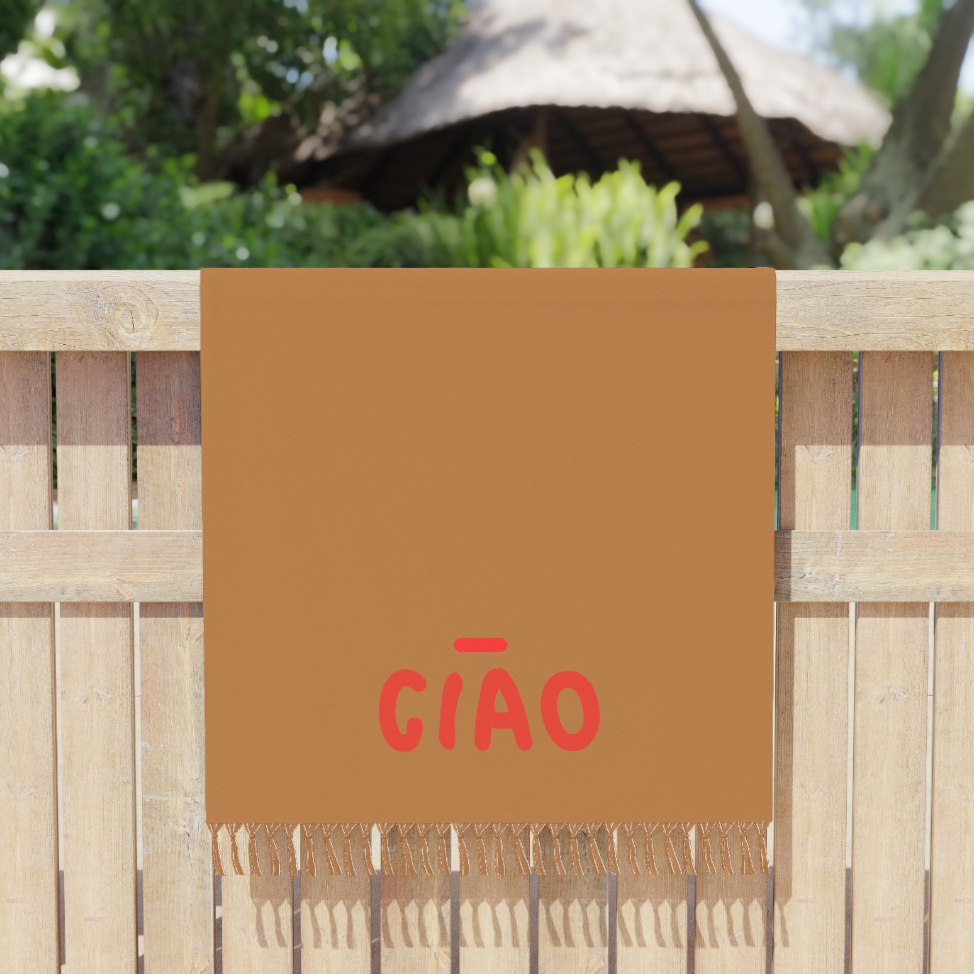 Brown towel with red text 'GIÓO' hanging on a wooden fence outdoors.