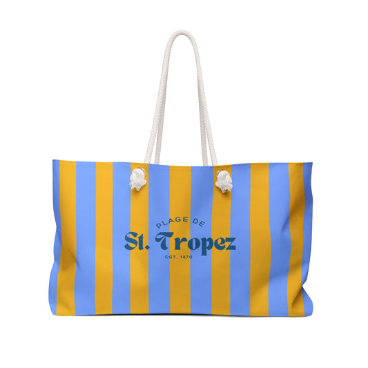 Striped bag with blue and yellow stripes and 'Plage de St. Tropez' text on a white background