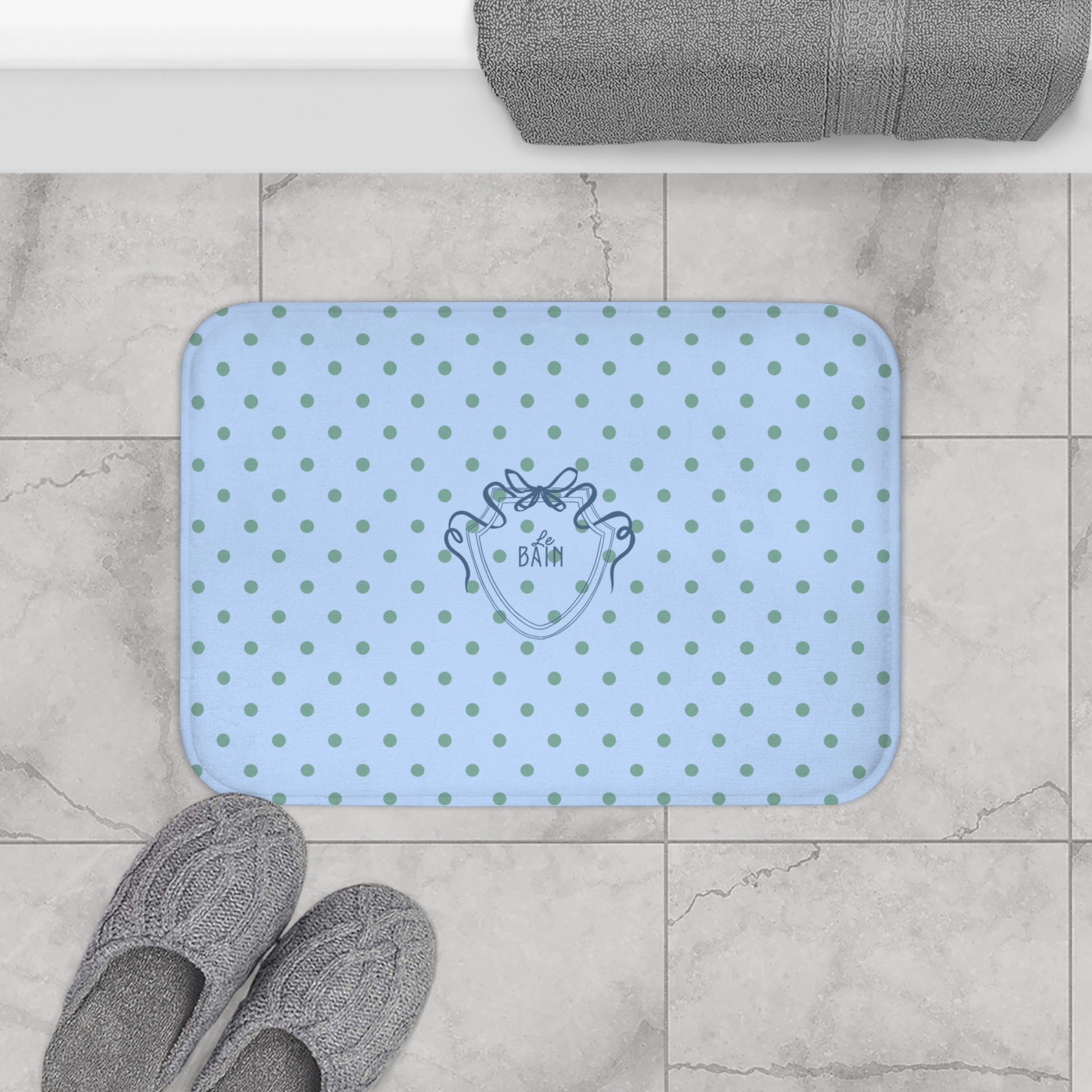 Blue polka dot bath mat with a cartoon frog design on a tiled bathroom floor.