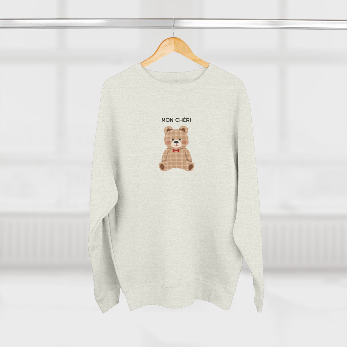 White sweater with a teddy bear design and 'MON CHÓRI' text on a white background