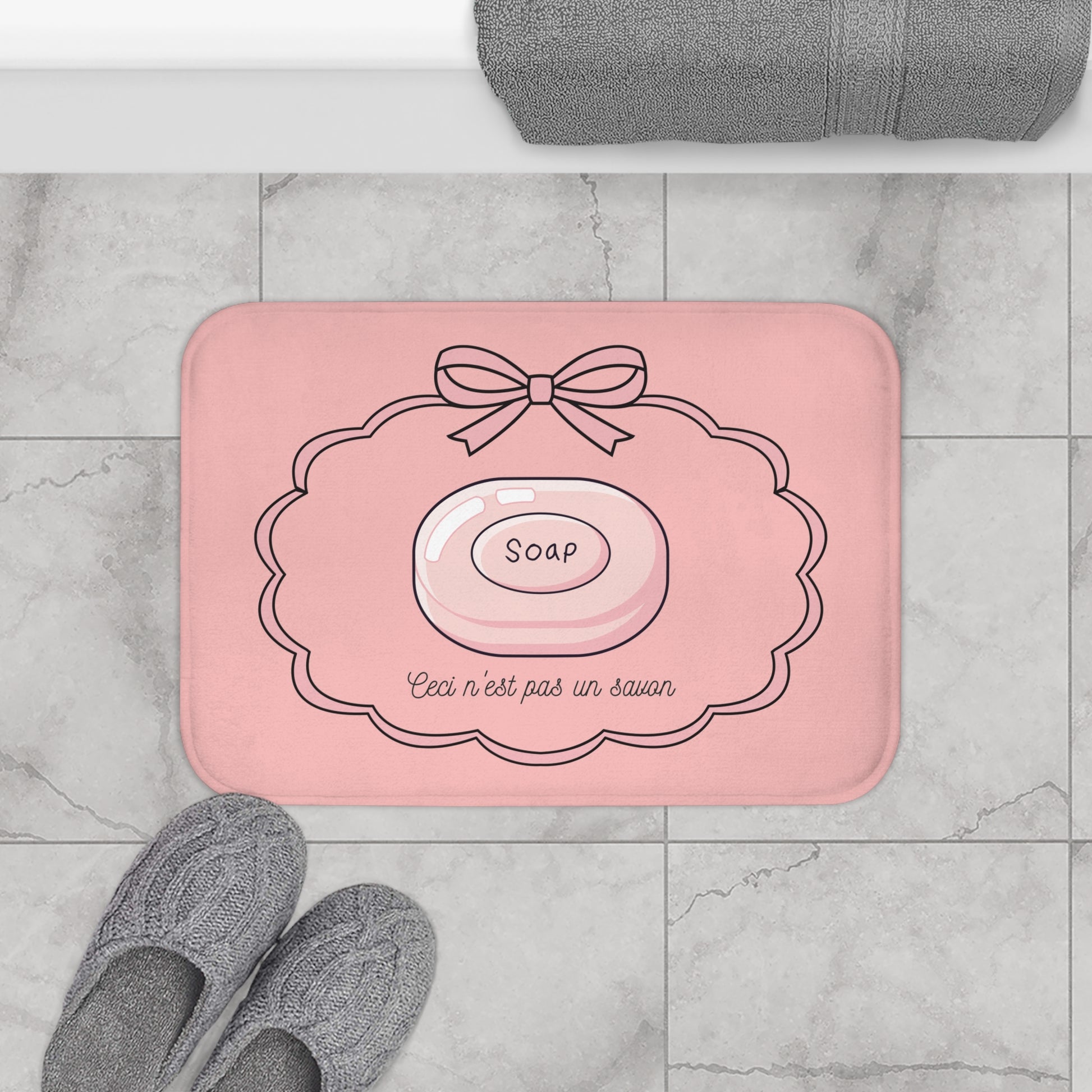 Pink bath mat with soap design on a marble floor with slippers and towel.