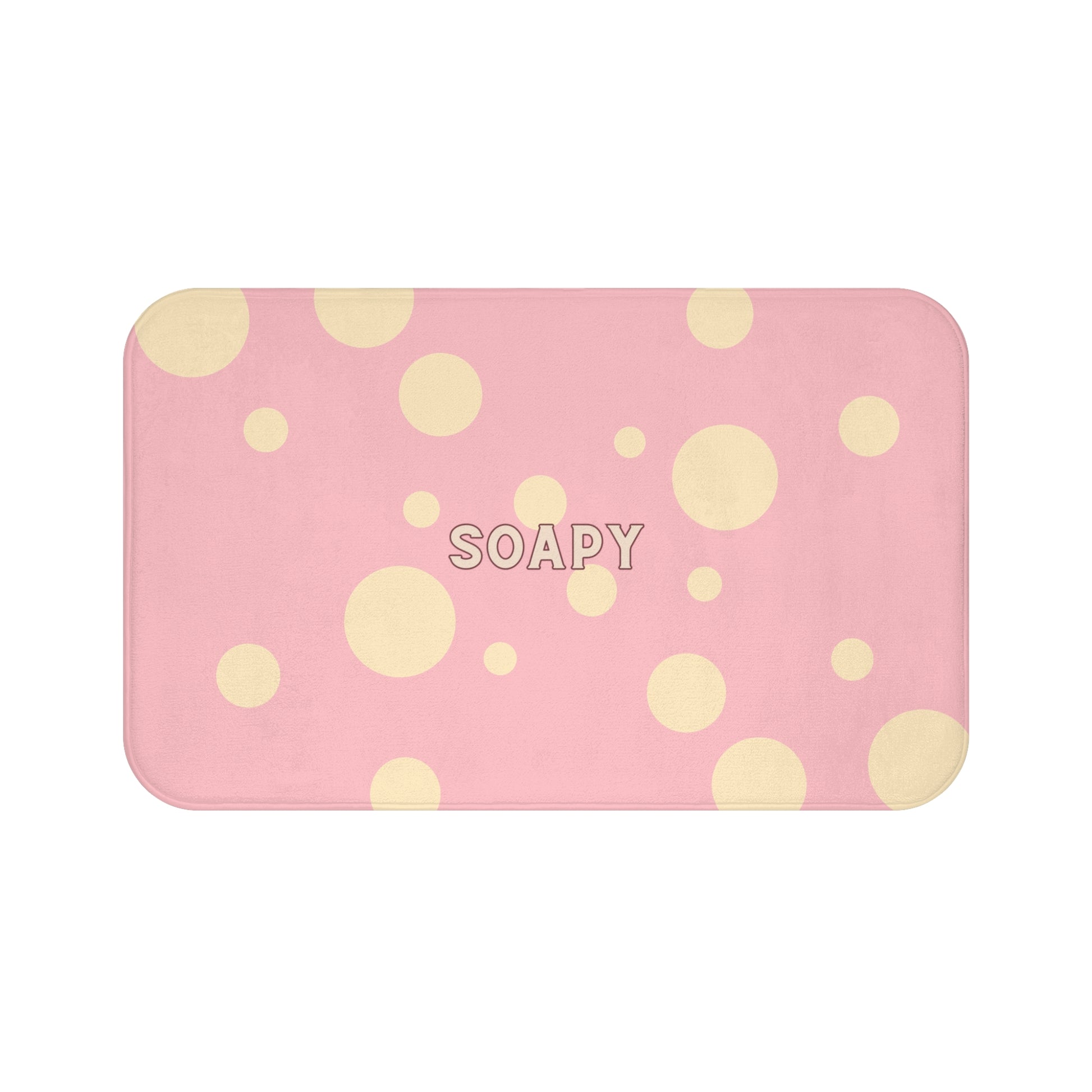 A rectangular pink bath mat with rounded corners, decorated with a pattern of light yellow polka dots and the word 'SOAPY' printed in the center, shown on a plain white background.