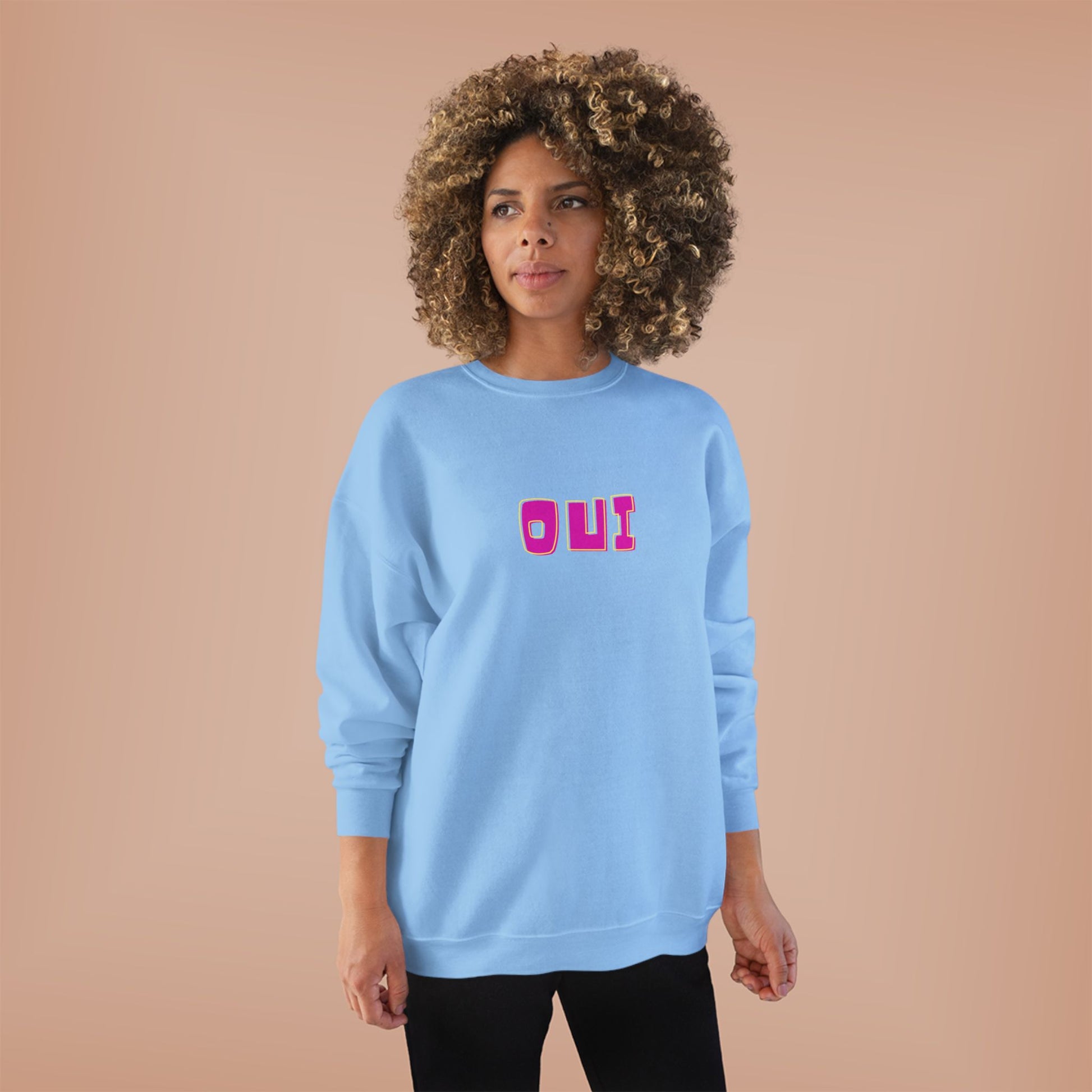Woman wearing a light blue sweatshirt with 'OUI' printed in pink on a beige background