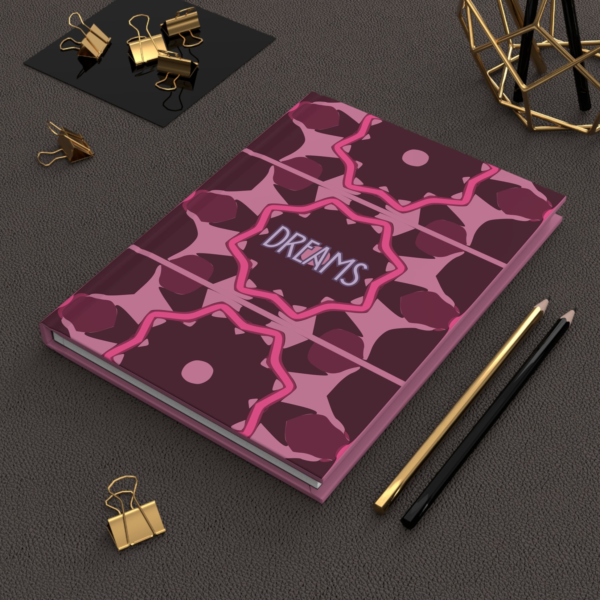 Purple notebook with geometric pattern and 'Dreams' text on a dark surface with office supplies.