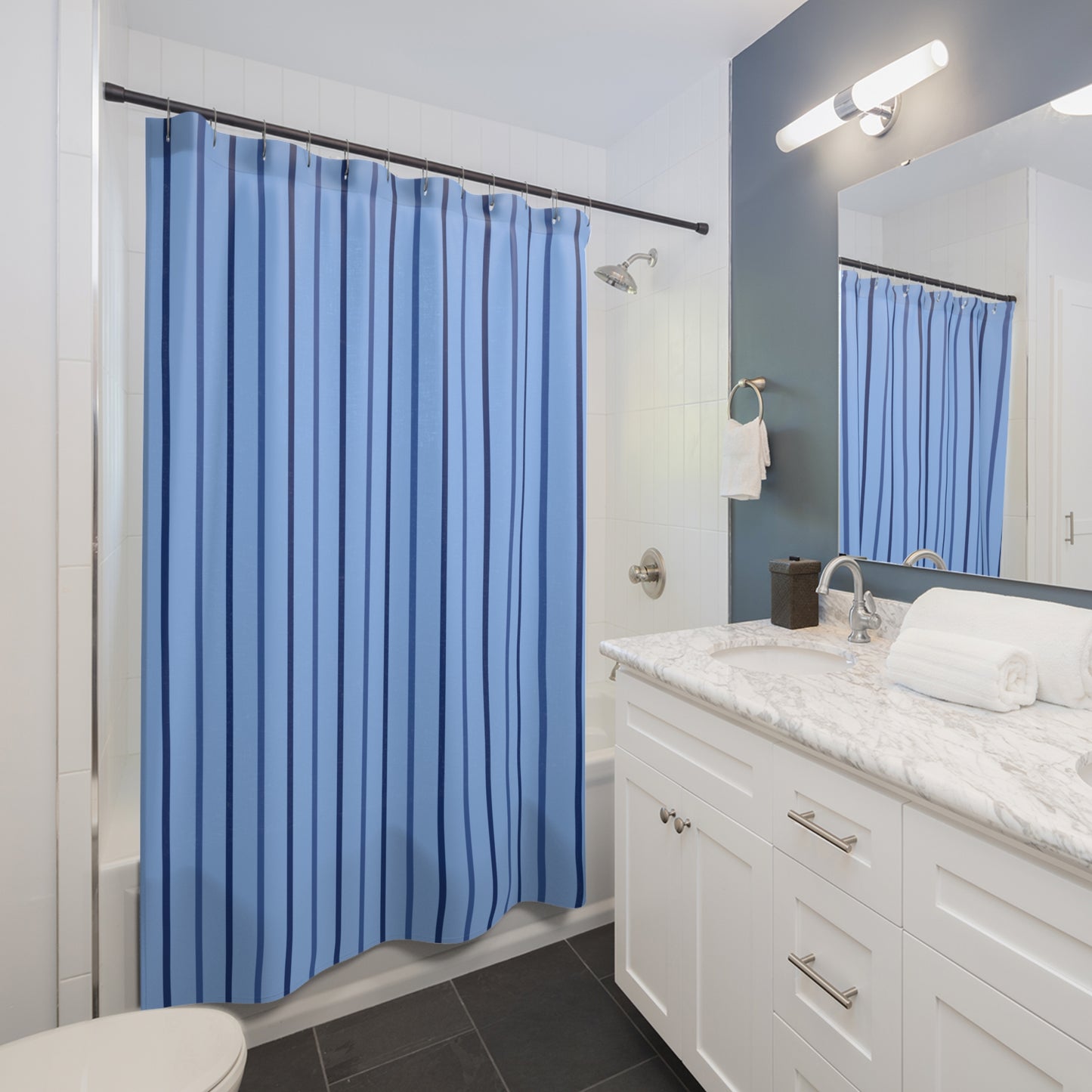 A blue shower curtain with vertical stripes hanging in a modern bathroom with white cabinets, a marble countertop, and a large mirror reflecting the curtain.