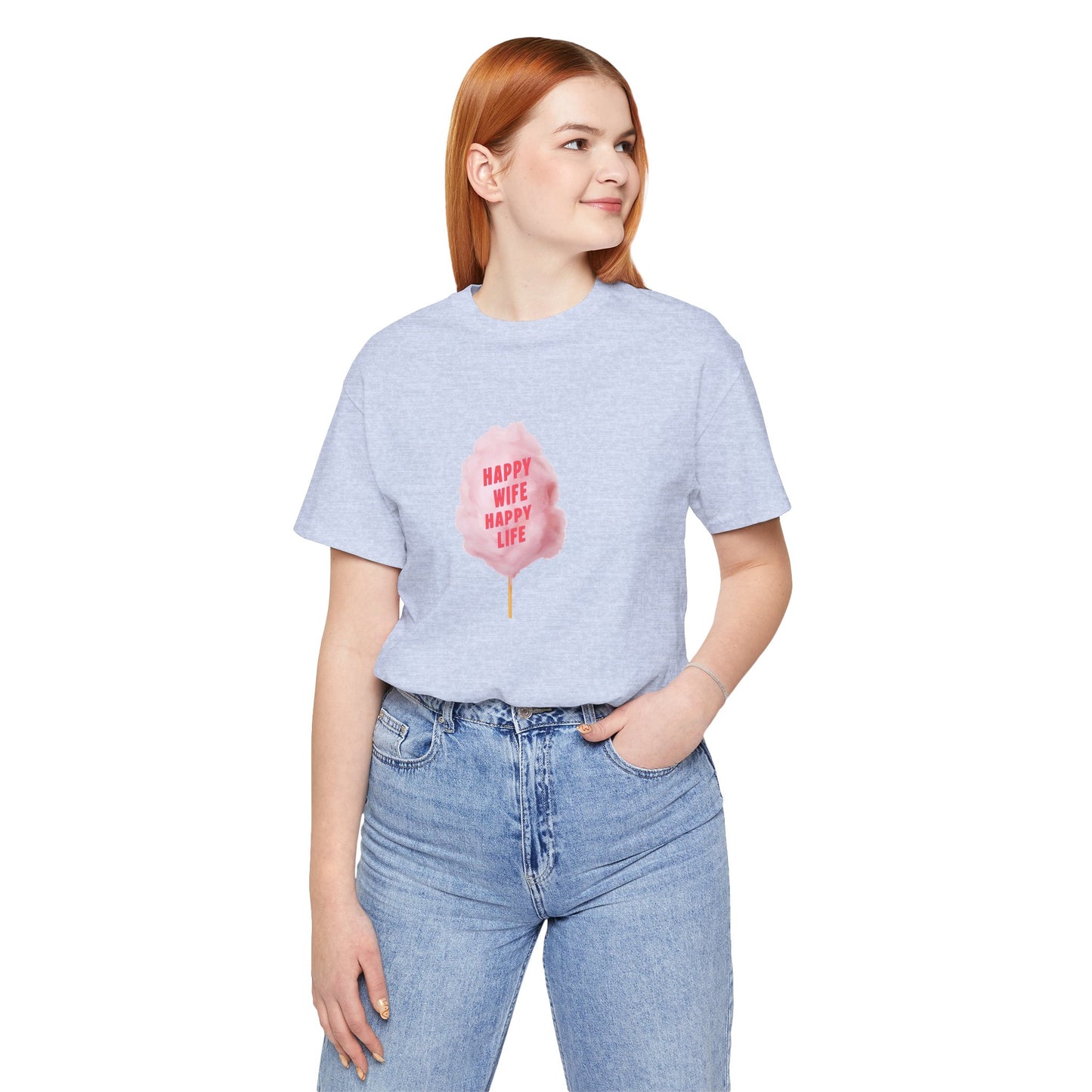 A woman with red hair wearing a light heather gray t-shirt with a pink cotton candy graphic that reads 'HAPPY WIFE HAPPY LIFE' and light wash blue jeans, standing against a solid white background.