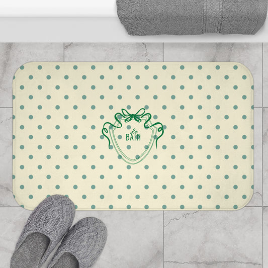 Beige bath mat with green polka dots and logo on a tiled bathroom floor.