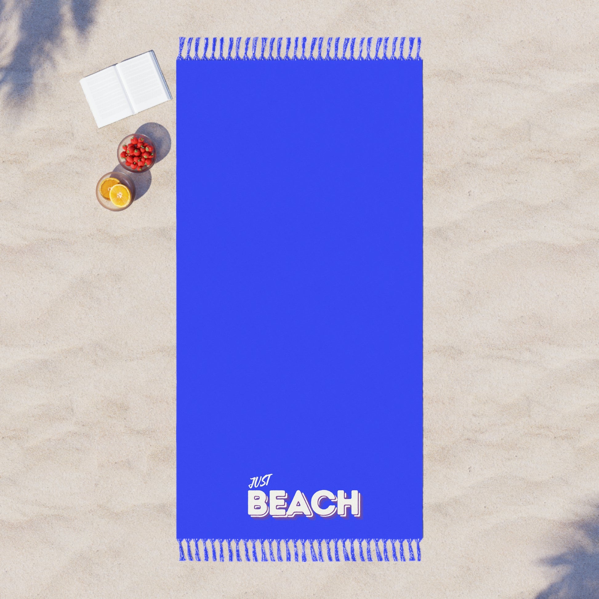 Blue beach towel with 'Just Beach' text on a sandy background