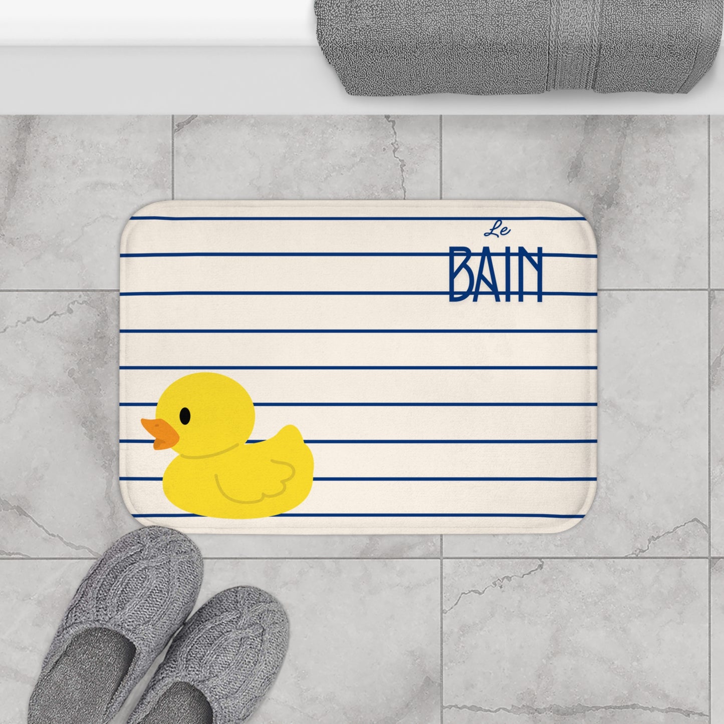 Bath mat with a rubber duck and 'Le Bain' text on a marble floor.