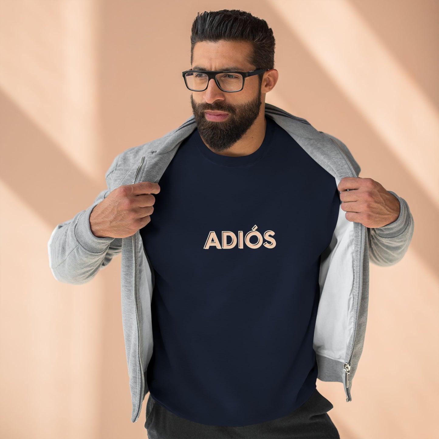 Man wearing a navy blue shirt with 'ADIóS' text and a gray jacket on a beige background