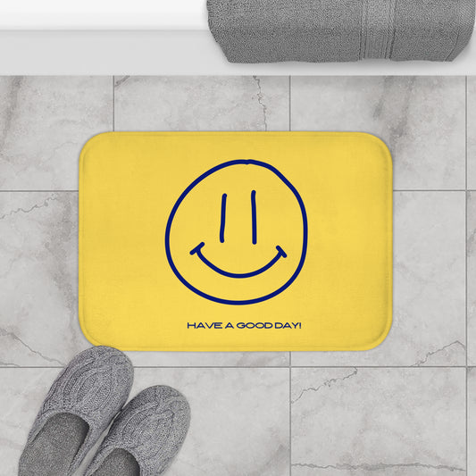 Yellow bath mat with blue smiley face and text 'Have a good day!' on a marble floor.