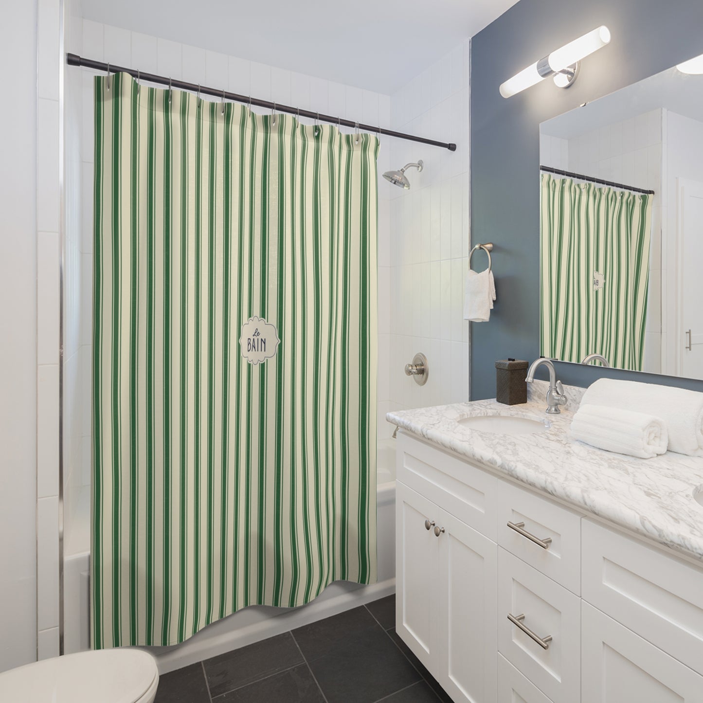 A bathroom scene showing a green and white vertically striped shower curtain hanging in a bathtub, with a white vanity, marble countertop, mirror, and wall light visible.