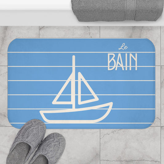 Blue bath mat with white sailboat design and 'Le Bain' text on a marble floor.