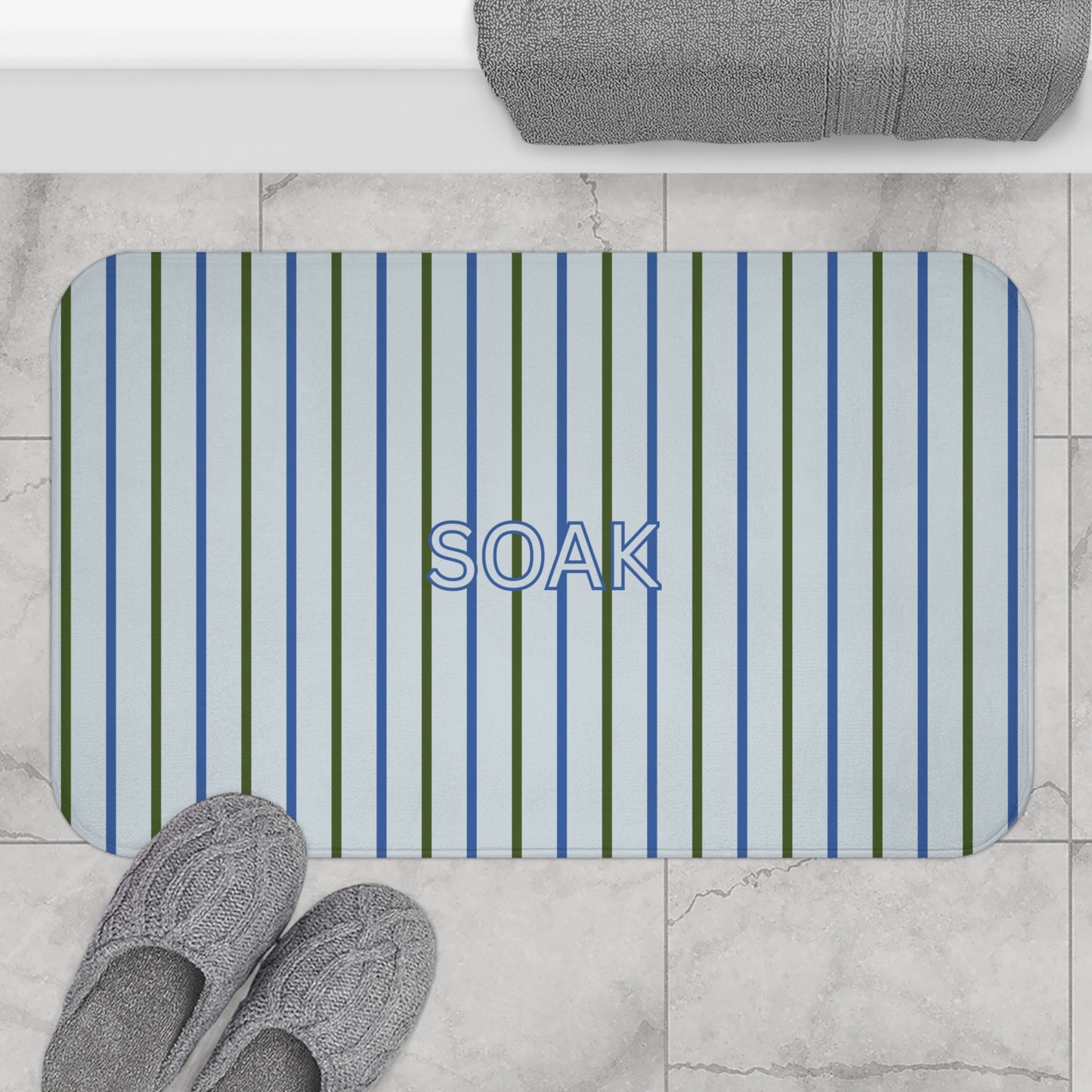 Striped bath mat with 'SOAK' text on a tiled bathroom floor.