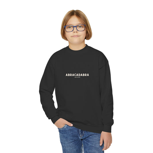 Child wearing a black sweatshirt with 'ABRACADABRA' text on a white background