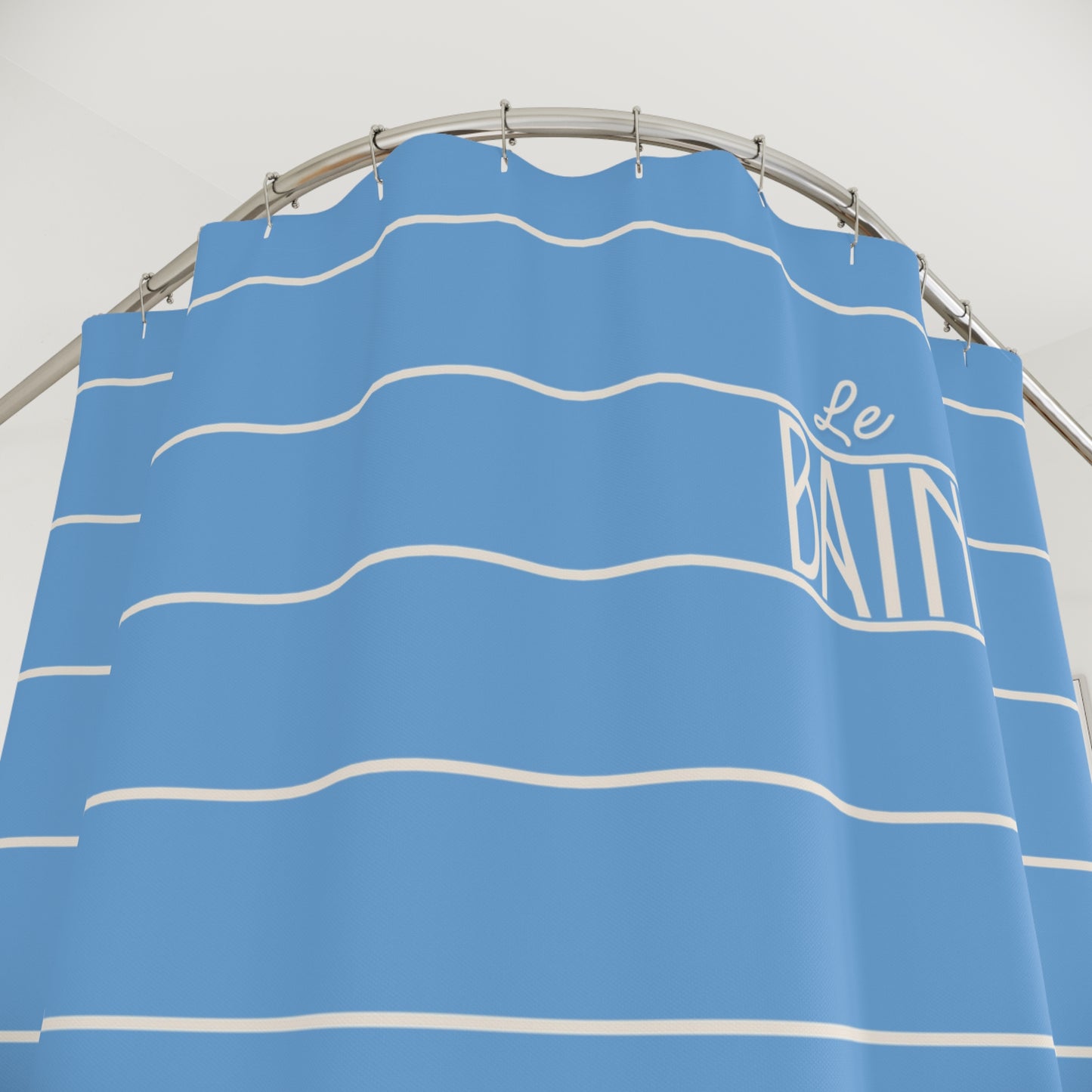 Blue shower curtain with white stripes and 'Le Bain' branding on a gray background