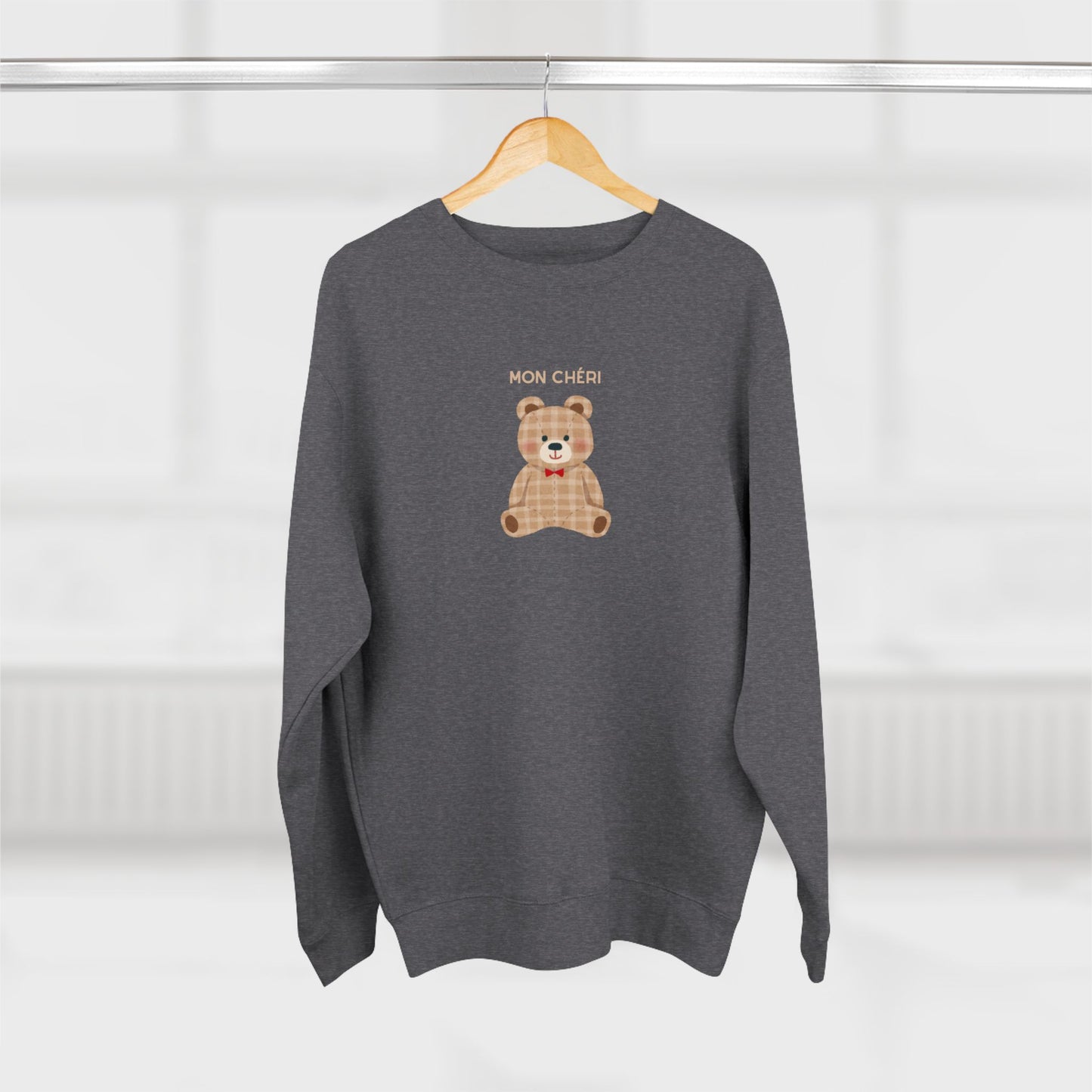 Gray sweater with a teddy bear design and text on a hanger against a white background