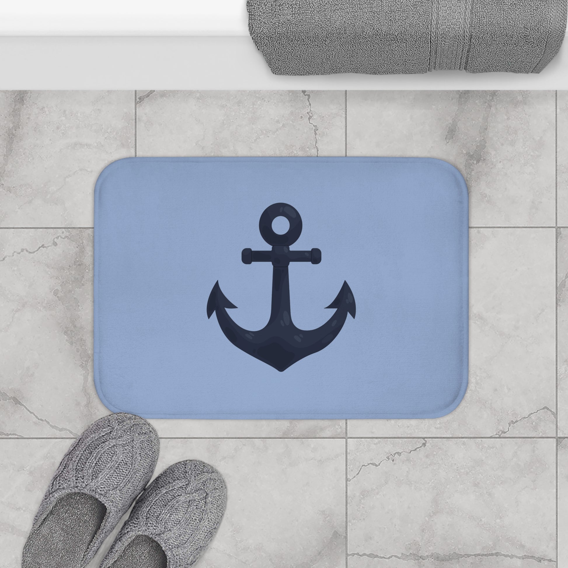 Blue bath mat with anchor design on a tiled bathroom floor.