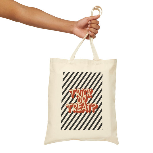 An off-white canvas tote bag with a 'Trick or Treat?' graphic, held by a person's arm against a solid white background.