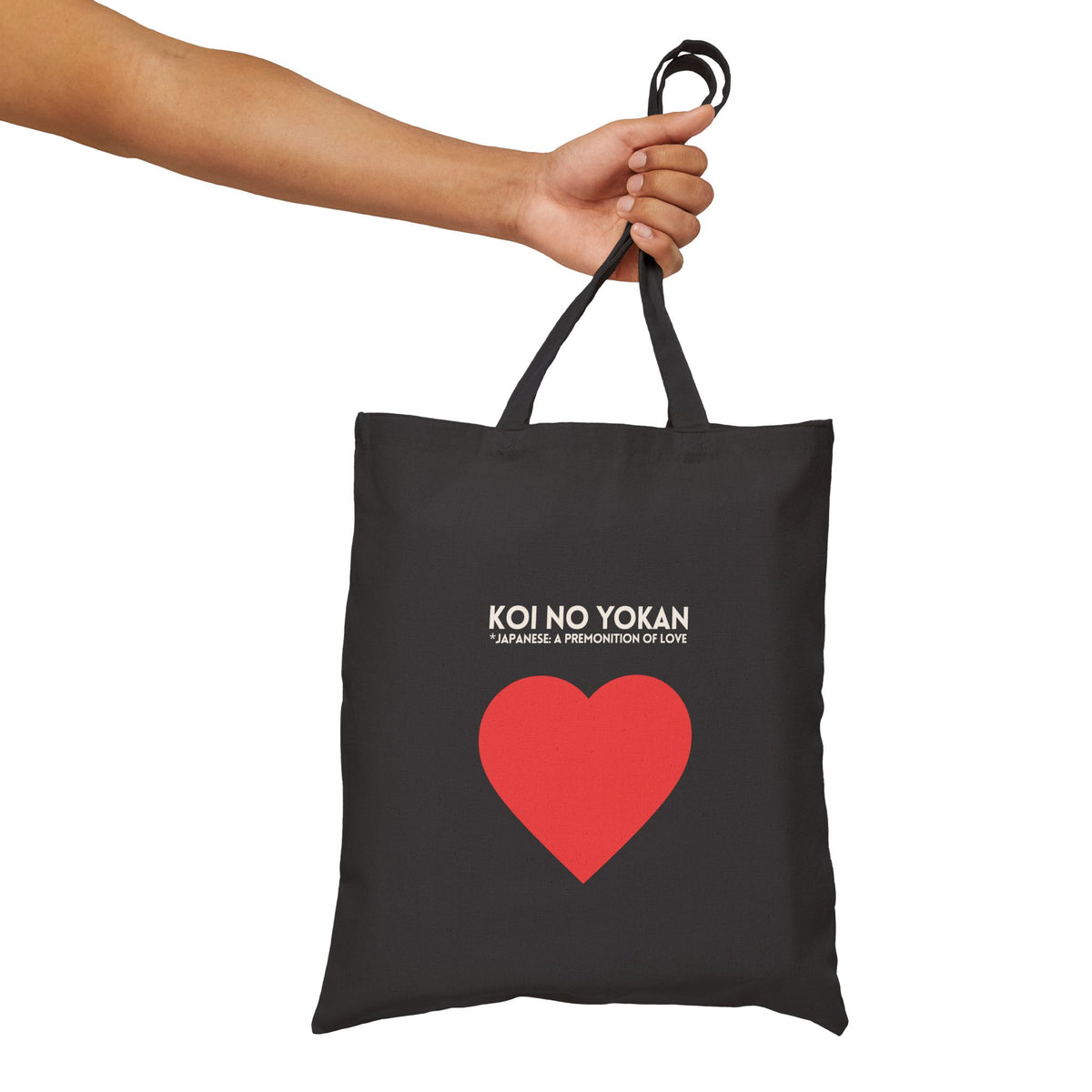 A black canvas tote bag with a red heart graphic and the text 'KOI NO YOKAN' and '*JAPANESE A PROPHETION OF LOVE' printed on the front, held by a person's arm against a plain white background.