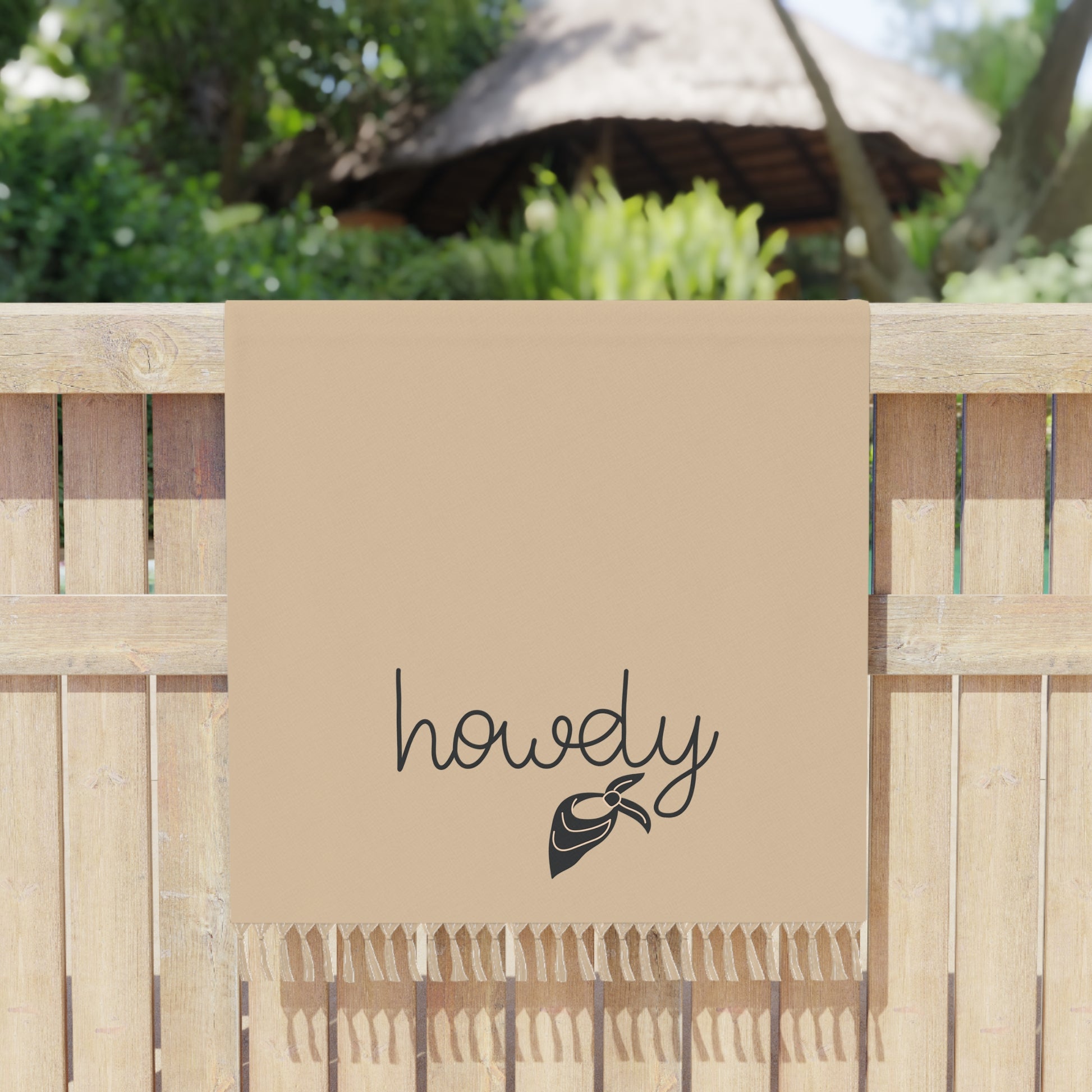 Beige towel with 'howdy' and a bow design on a wooden fence background
