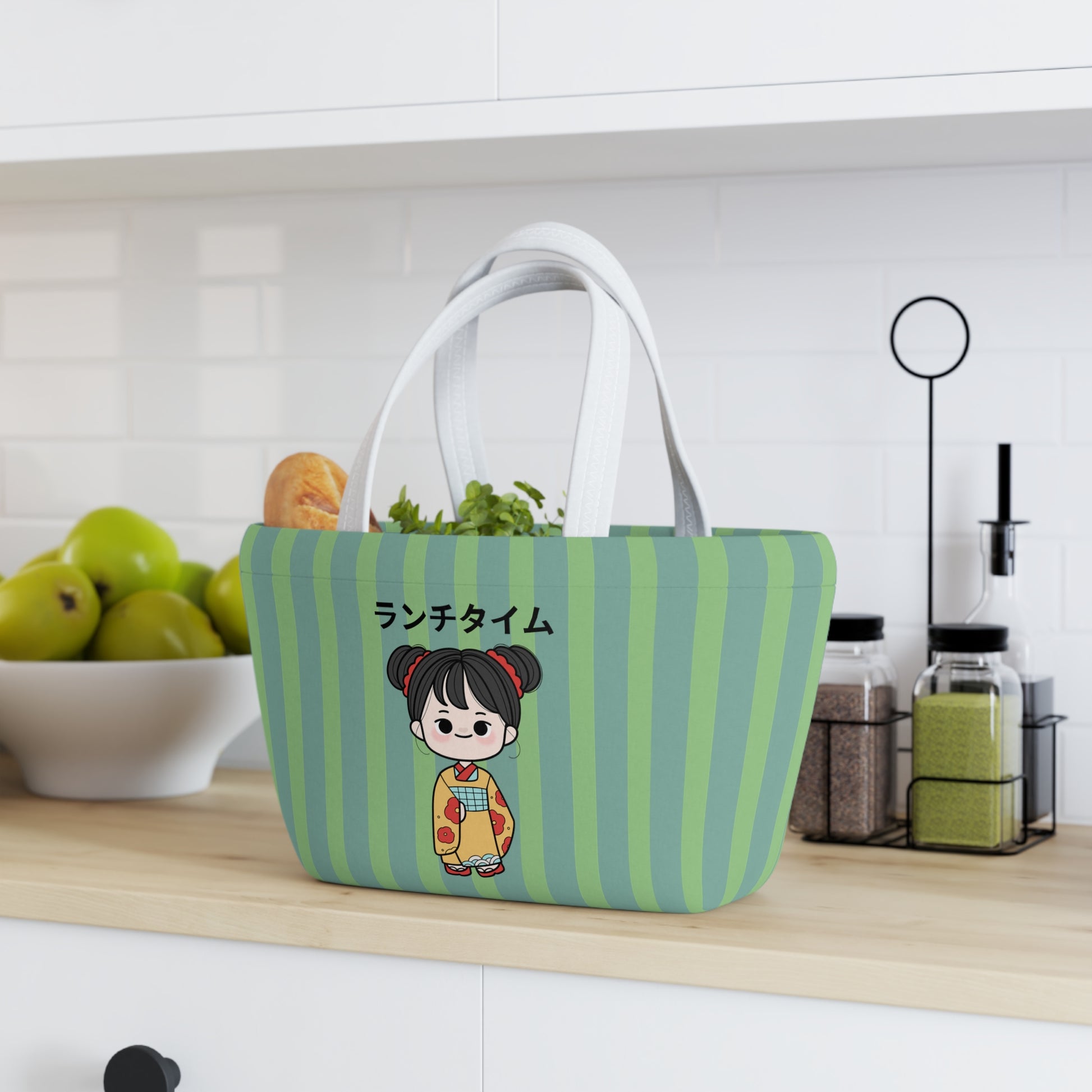 A green and light blue striped fabric lunch bag with white handles sits on a kitchen counter, filled with leafy greens. The front features a cartoon girl in a kimono with Japanese text.