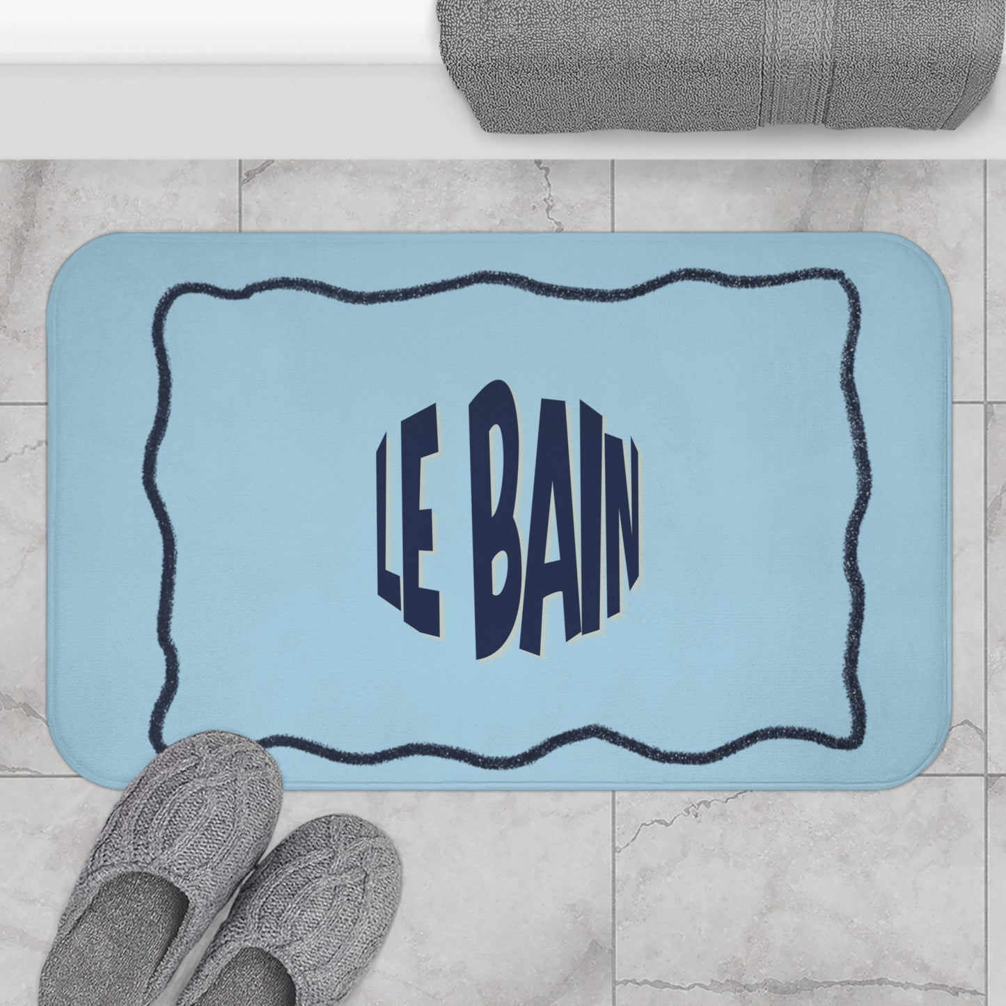 Blue bath mat with 'LE BAIN' text on a bathroom floor.